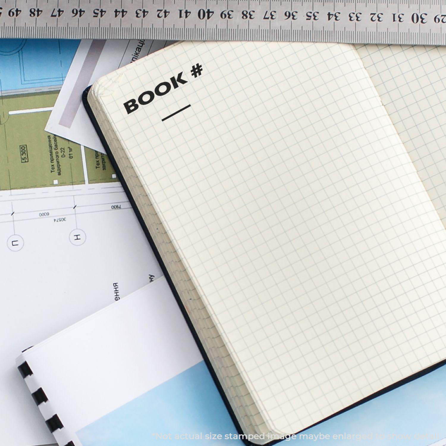 Large Book Rubber Stamp used on an open notebook with grid paper, next to a ruler and other stationery items.