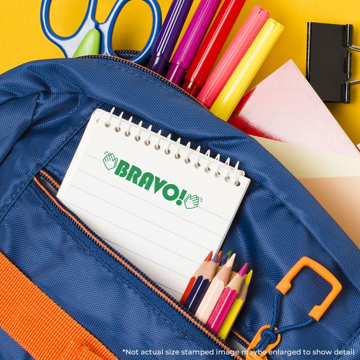 Blue backpack with colored pencils, scissors, and a notepad stamped with Bravo with Hands Rubber Stamp in green ink.