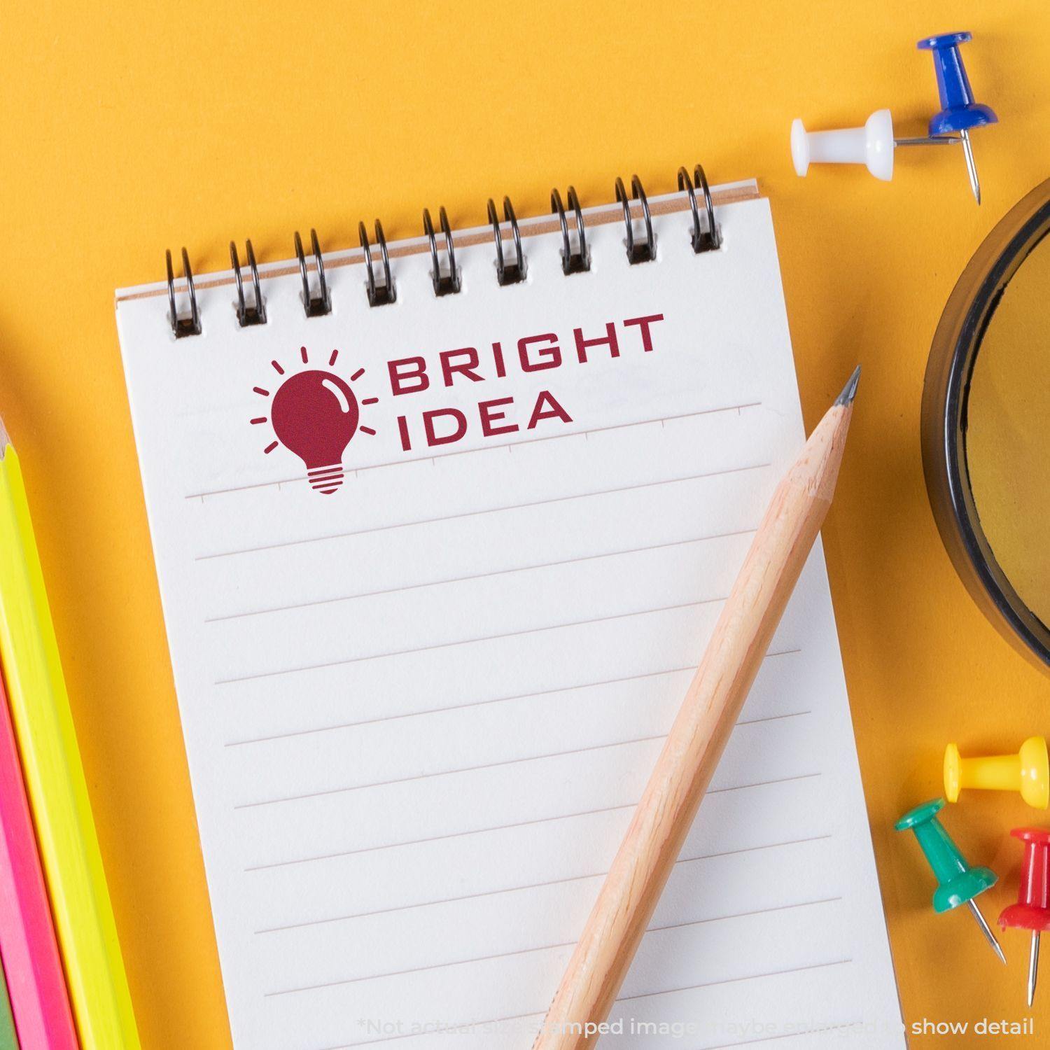 Notepad with a Bright Idea rubber stamp impression, pencil, colorful push pins, and a yellow background.