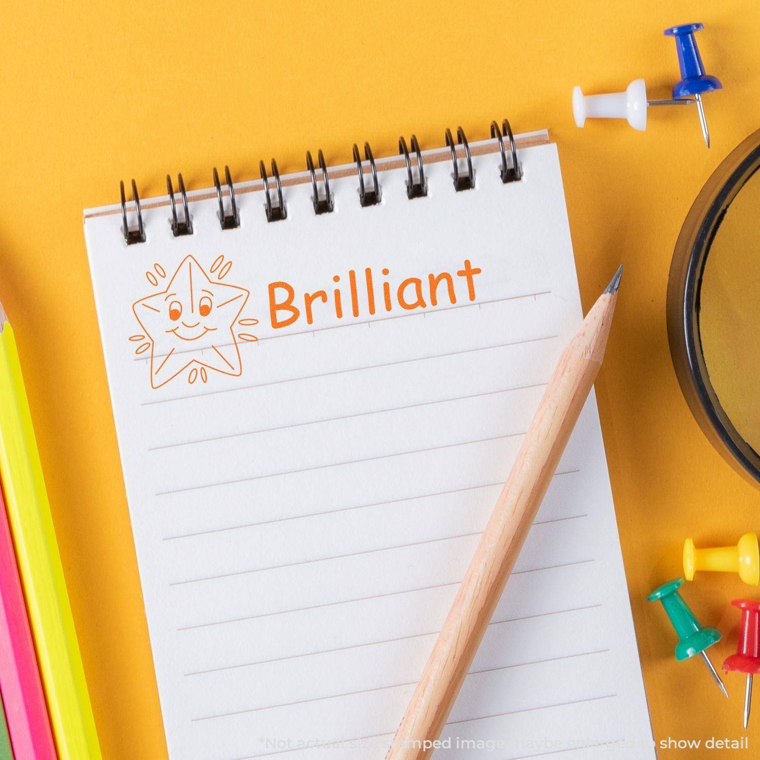 Brilliant rubber stamp on a notepad with a smiling star, surrounded by colorful pencils, push pins, and a pencil.