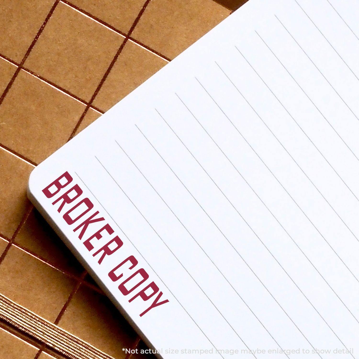 Self Inking Broker Copy Stamp marking BROKER COPY in red on a lined notepad, placed on a brown checkered surface.