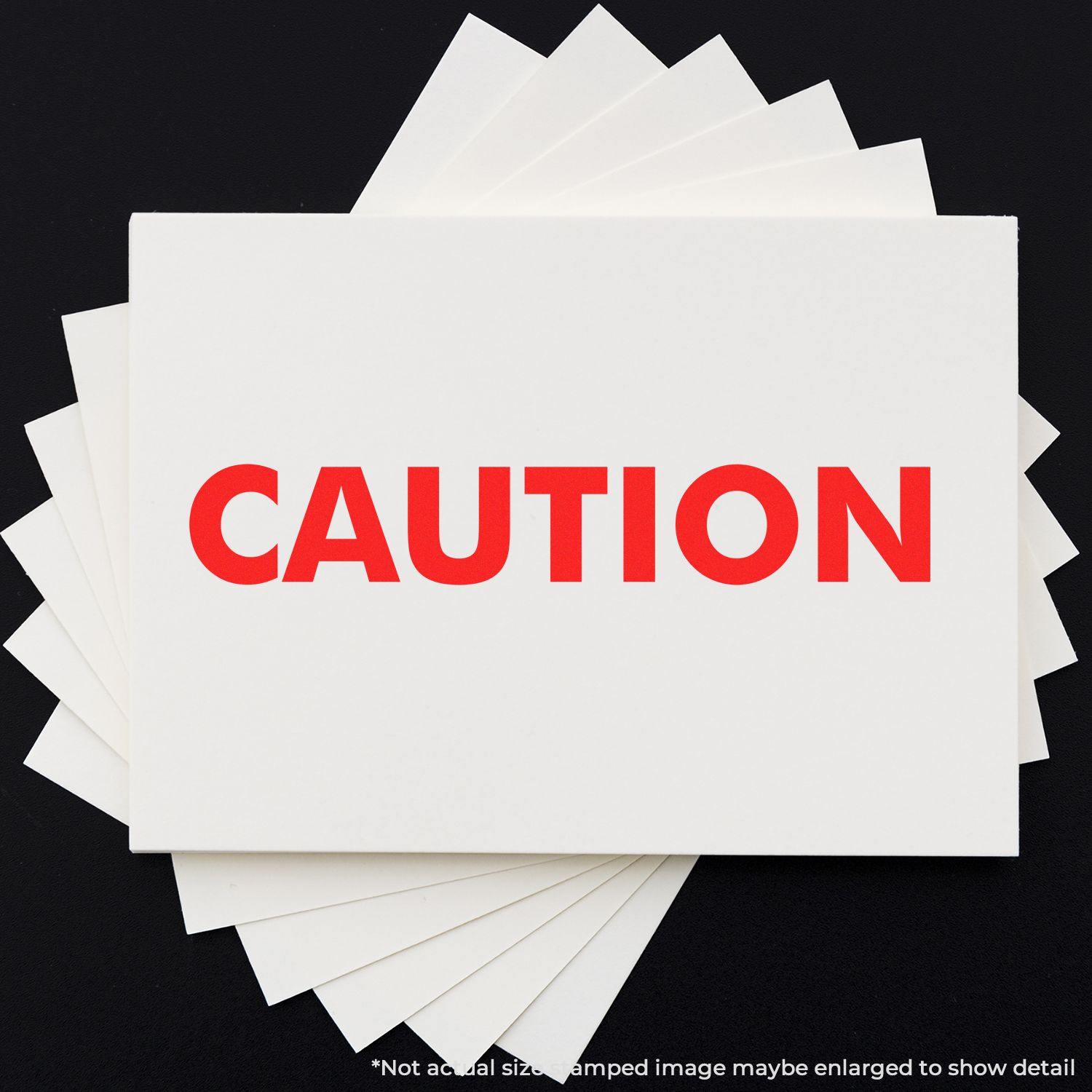 Large Caution Rubber Stamp in use, displaying the word CAUTION in bold red letters on white paper against a black background.