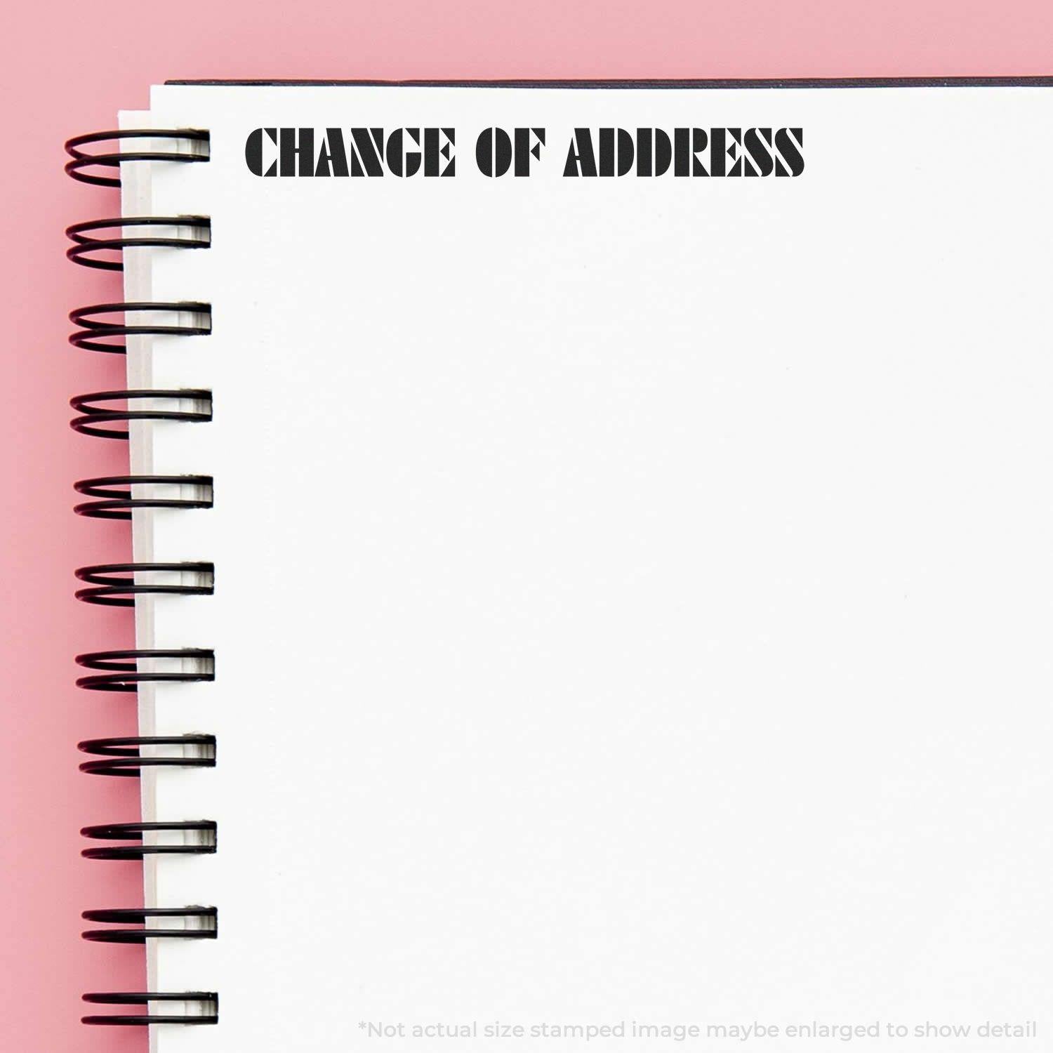 Large Pre-Inked Change Of Address Stamp used on a spiral-bound notebook with CHANGE OF ADDRESS stamped in bold black letters on a white page.