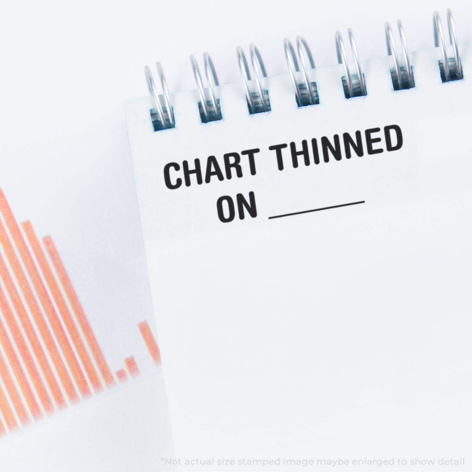 Self Inking Chart Thinned On Stamp used on a spiral-bound notebook with a chart in the background.