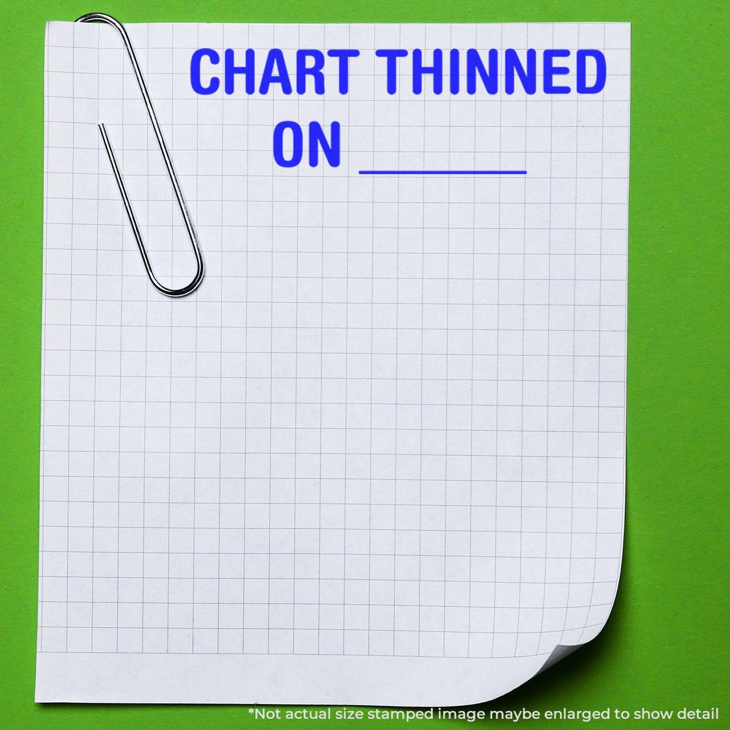 A Large Chart Thinned On Rubber Stamp impression on a grid paper with a paperclip, placed on a green background.