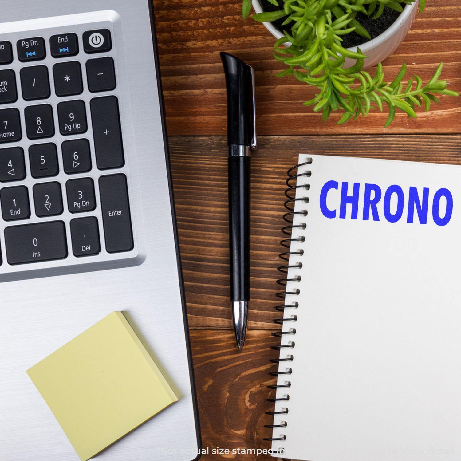 Self Inking Chrono Stamp next to a laptop, pen, sticky notes, and a notebook with CHRONO written on it, placed on a wooden desk.