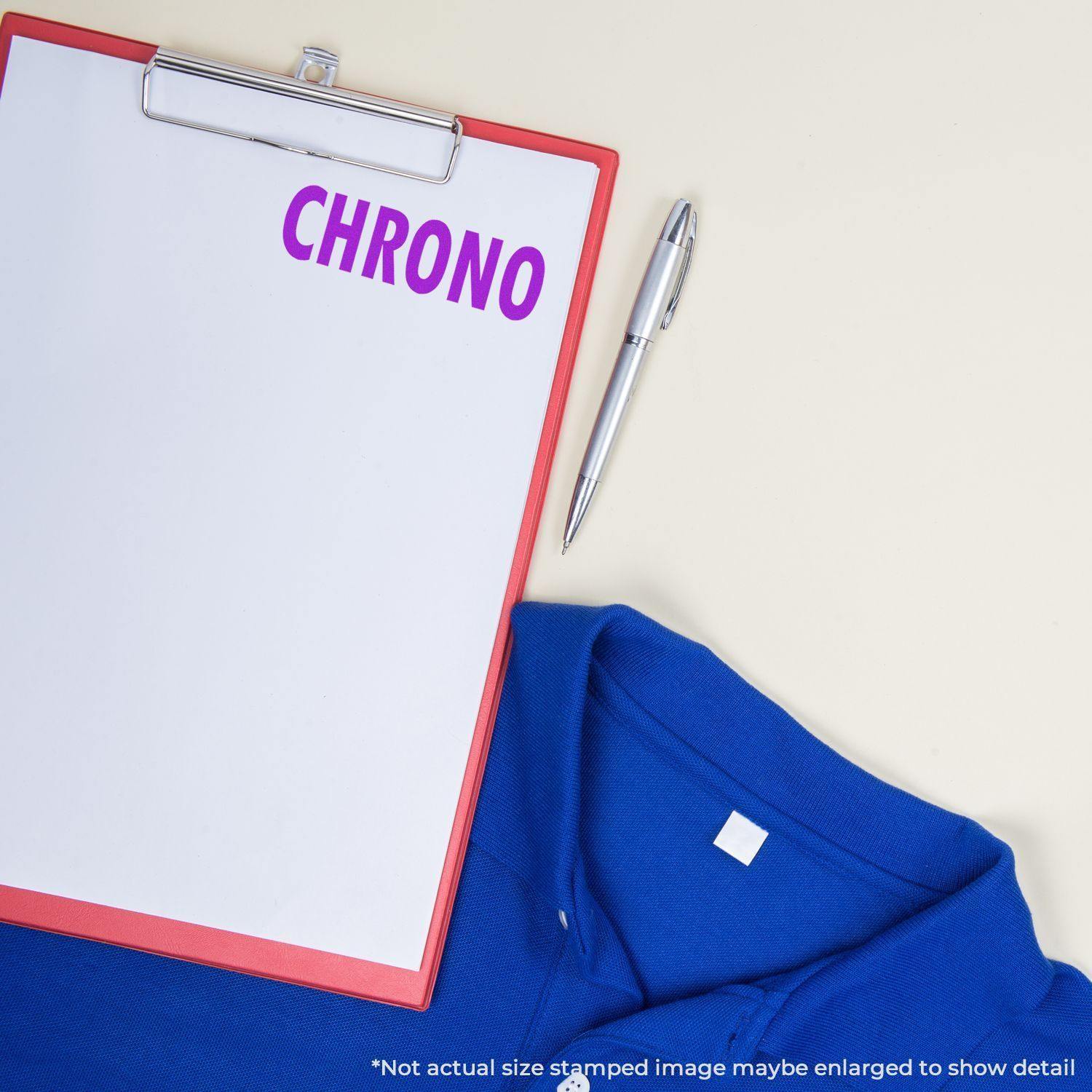 Clipboard with CHRONO stamped in purple using the Chrono Rubber Stamp, next to a silver pen and a blue shirt on a light background.