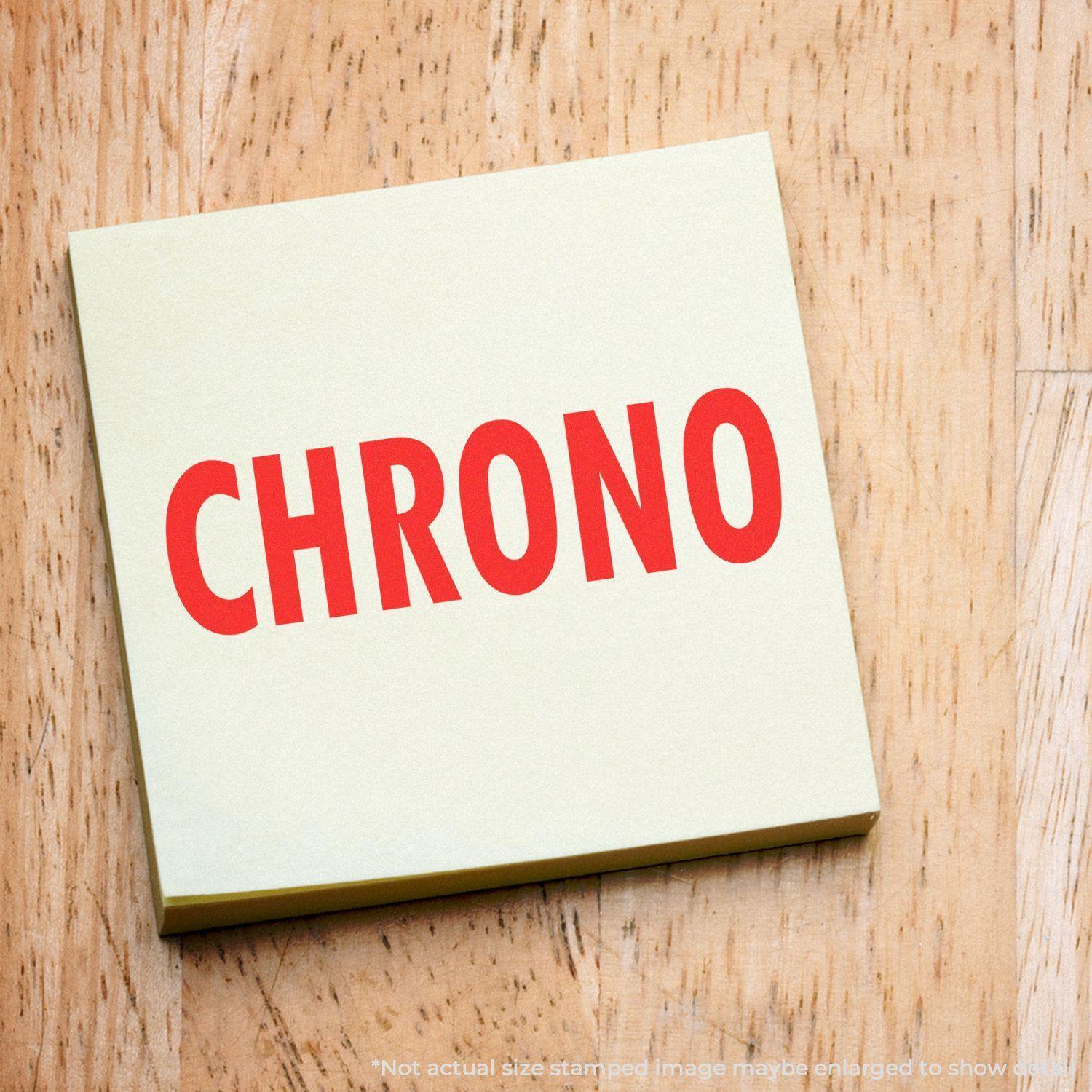 Chrono Rubber Stamp imprint in bold red letters on a yellow sticky note, placed on a wooden surface.