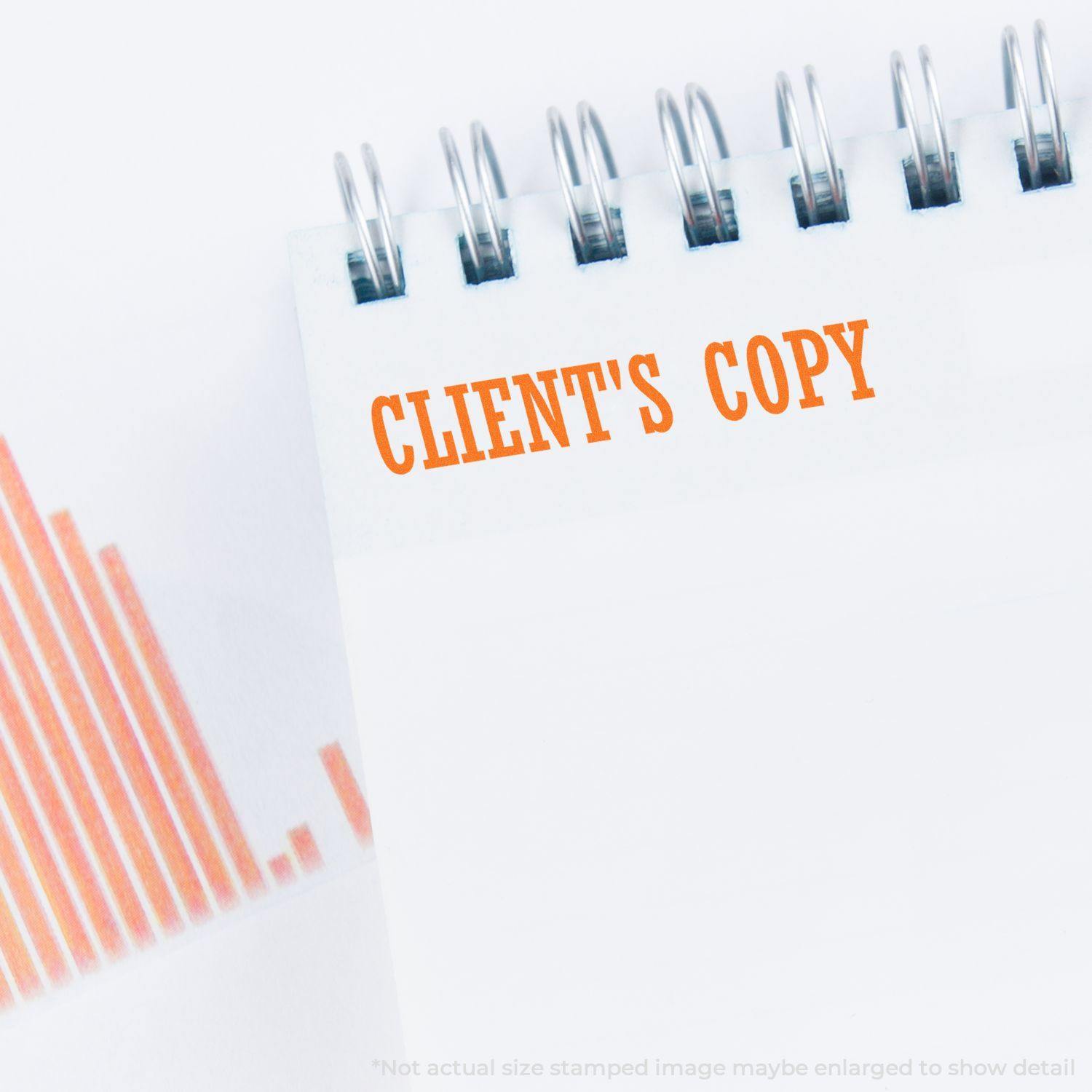 A spiral notebook with CLIENT'S COPY stamped in orange using the Clients Copy Rubber Stamp, next to an orange bar graph.