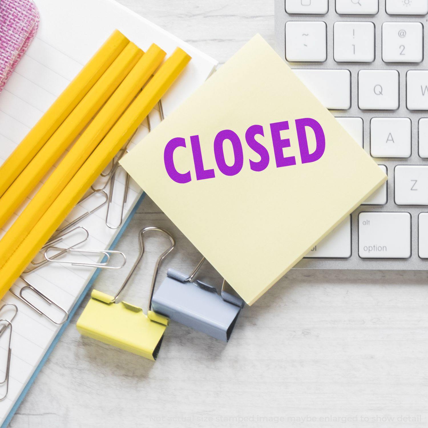 Large Pre-Inked Closed Stamp on a desk with pencils, paper clips, binder clips, and a keyboard in the background.