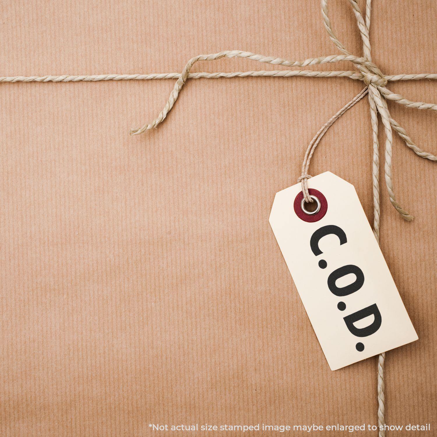 A Large Pre-Inked C.O.D. Stamp is used on a brown paper package tied with string, with a C.O.D. tag attached.