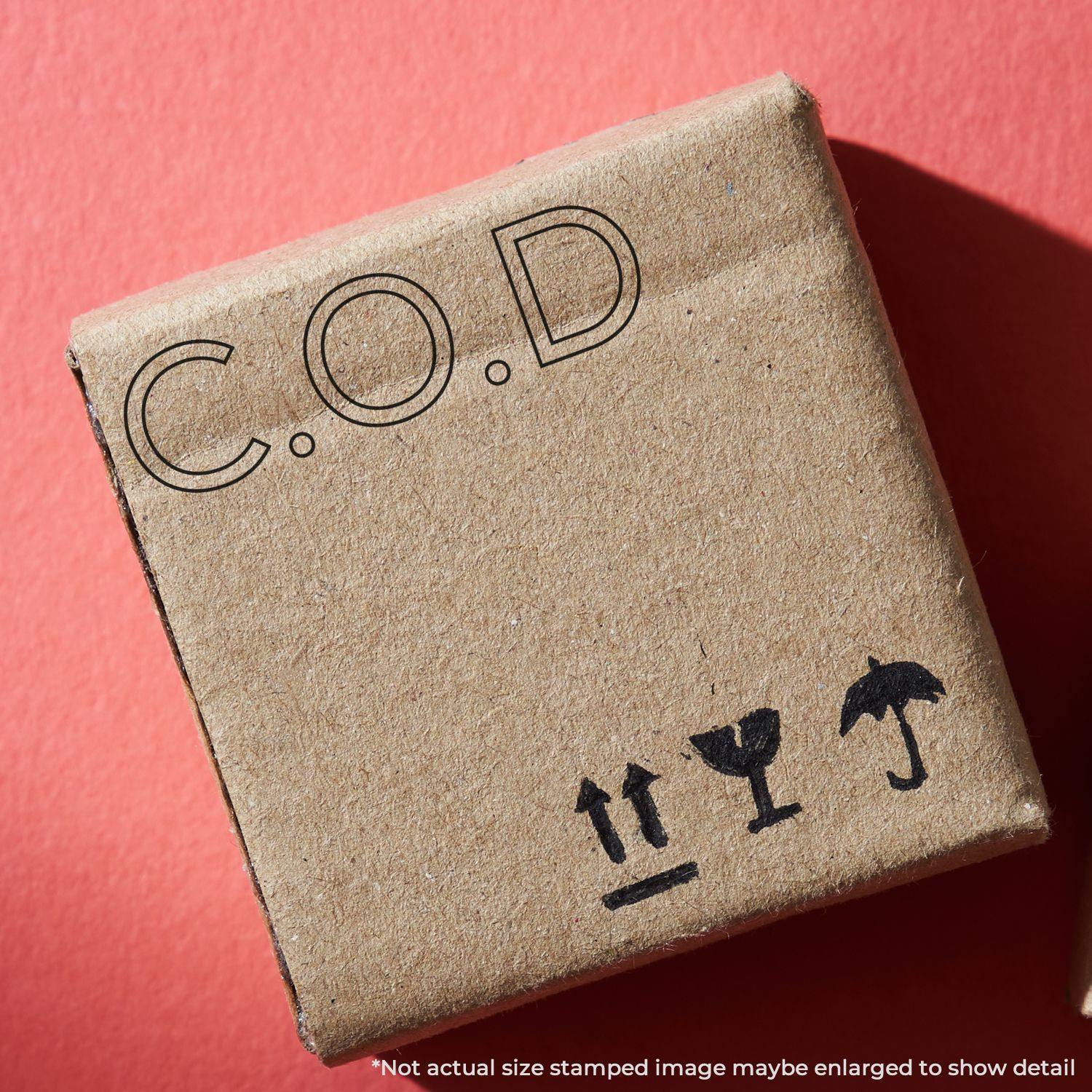 A cardboard box stamped with C.O.D using the Large Pre-Inked COD Outline Stamp, placed on a red background.