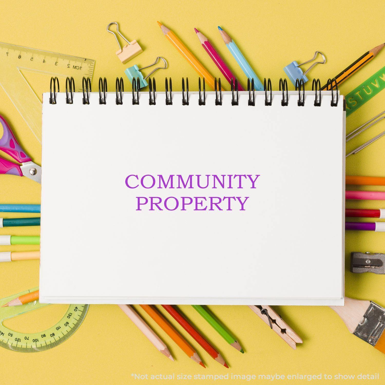 Large Community Property Rubber Stamp used on a white notebook surrounded by colorful stationery on a yellow background.