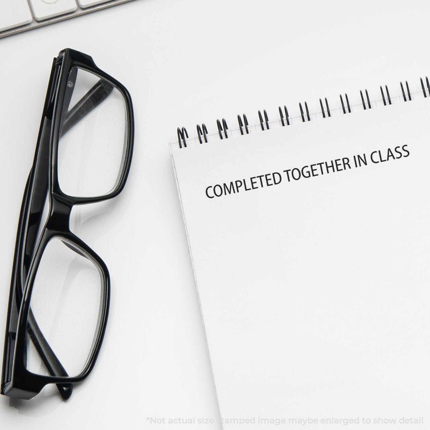 A pair of glasses next to a notebook stamped with COMPLETED TOGETHER IN CLASS using the Large Completed Together In Class Rubber Stamp.