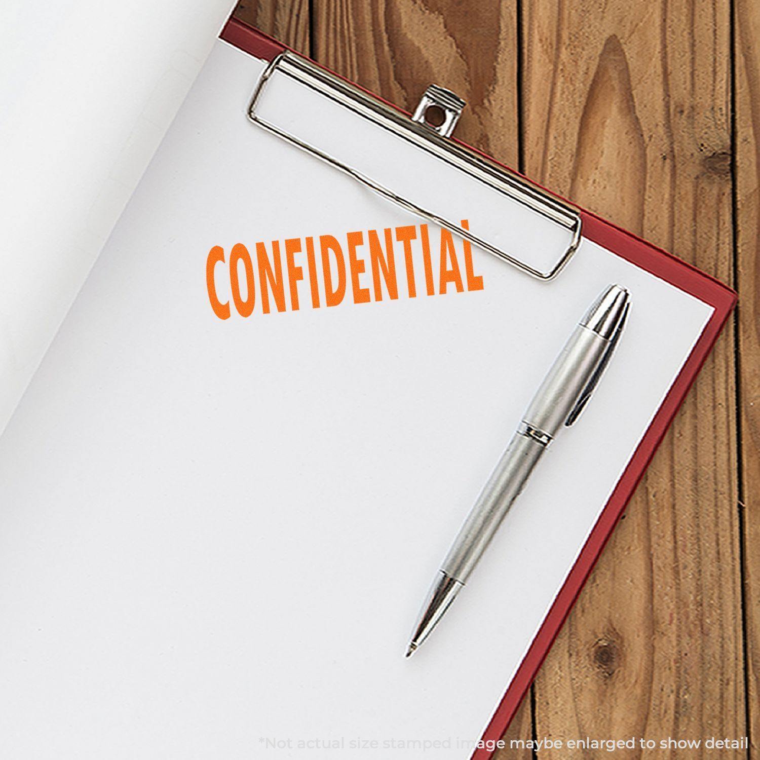 A clipboard with a paper stamped CONFIDENTIAL using the Confidential Rubber Stamp, next to a silver pen on a wooden surface.