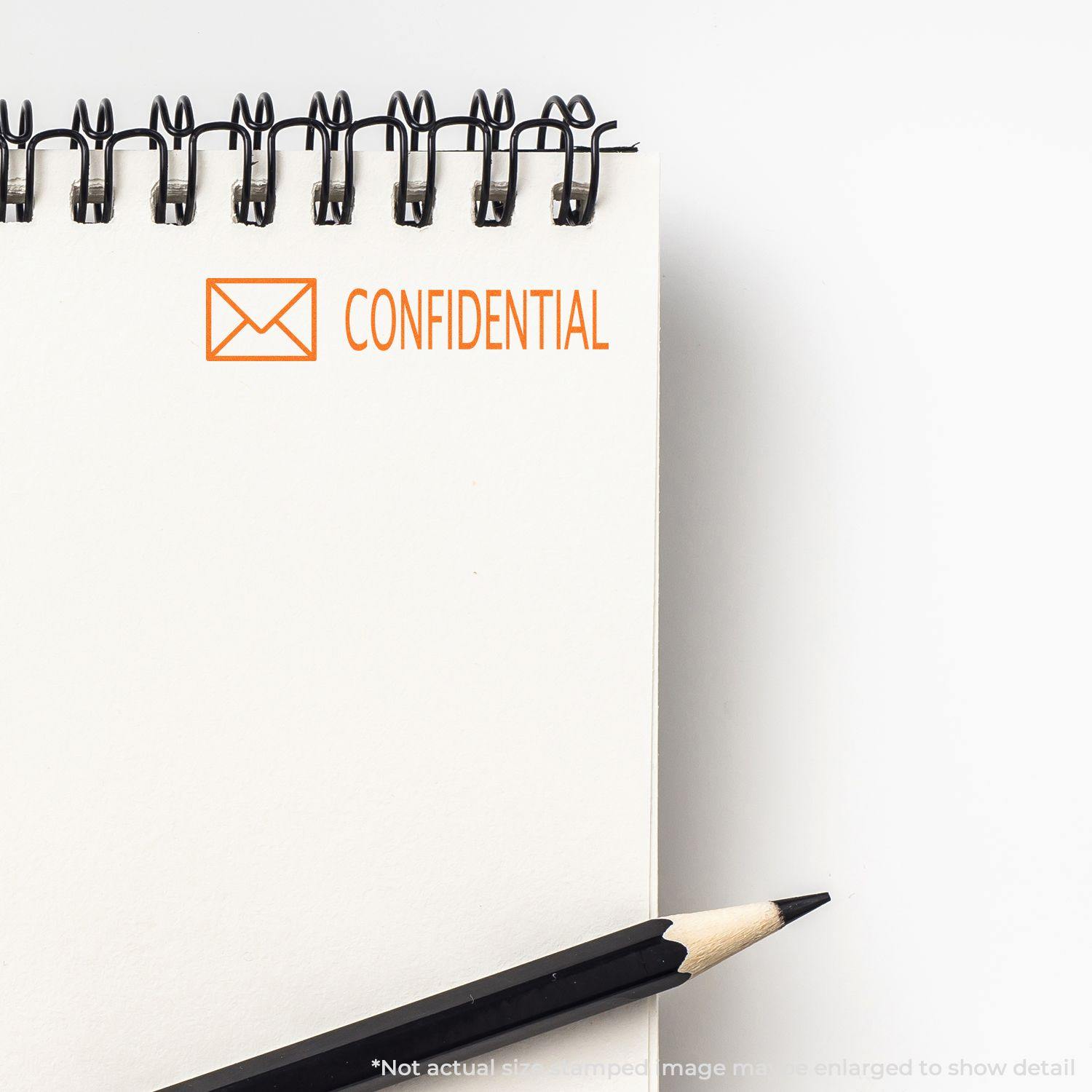 Large Confidential with Envelope Rubber Stamp marking a spiral notebook page, with a pencil placed beside the notebook.