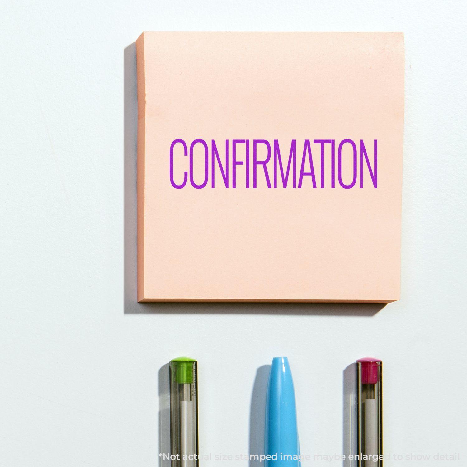 Large Confirmation Rubber Stamp used on a pink sticky note with the word CONFIRMATION in purple, placed above three pens.