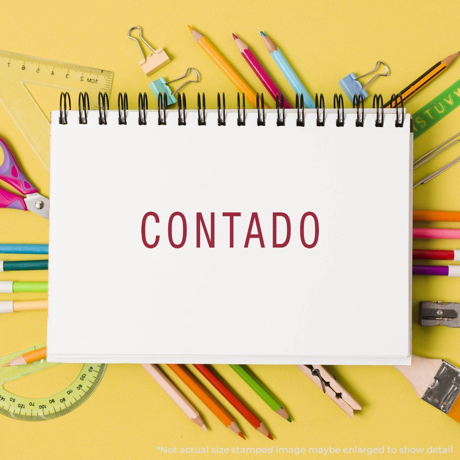 Large Pre-Inked Contado Stamp used on a white notebook surrounded by colorful stationery on a yellow background.