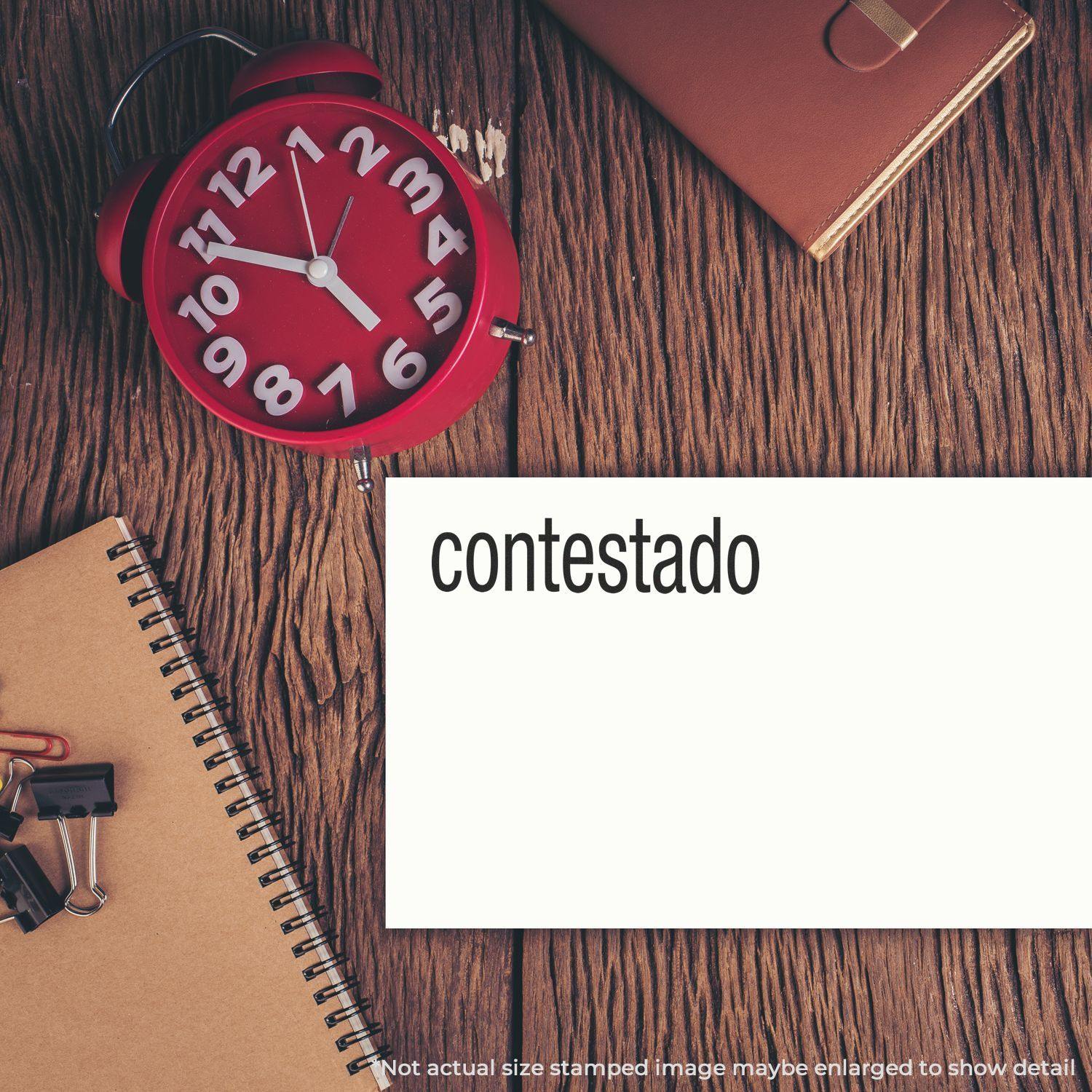 Large Contestado Rubber Stamp used on a white card, placed on a wooden desk with a red clock, notebook, and office supplies.