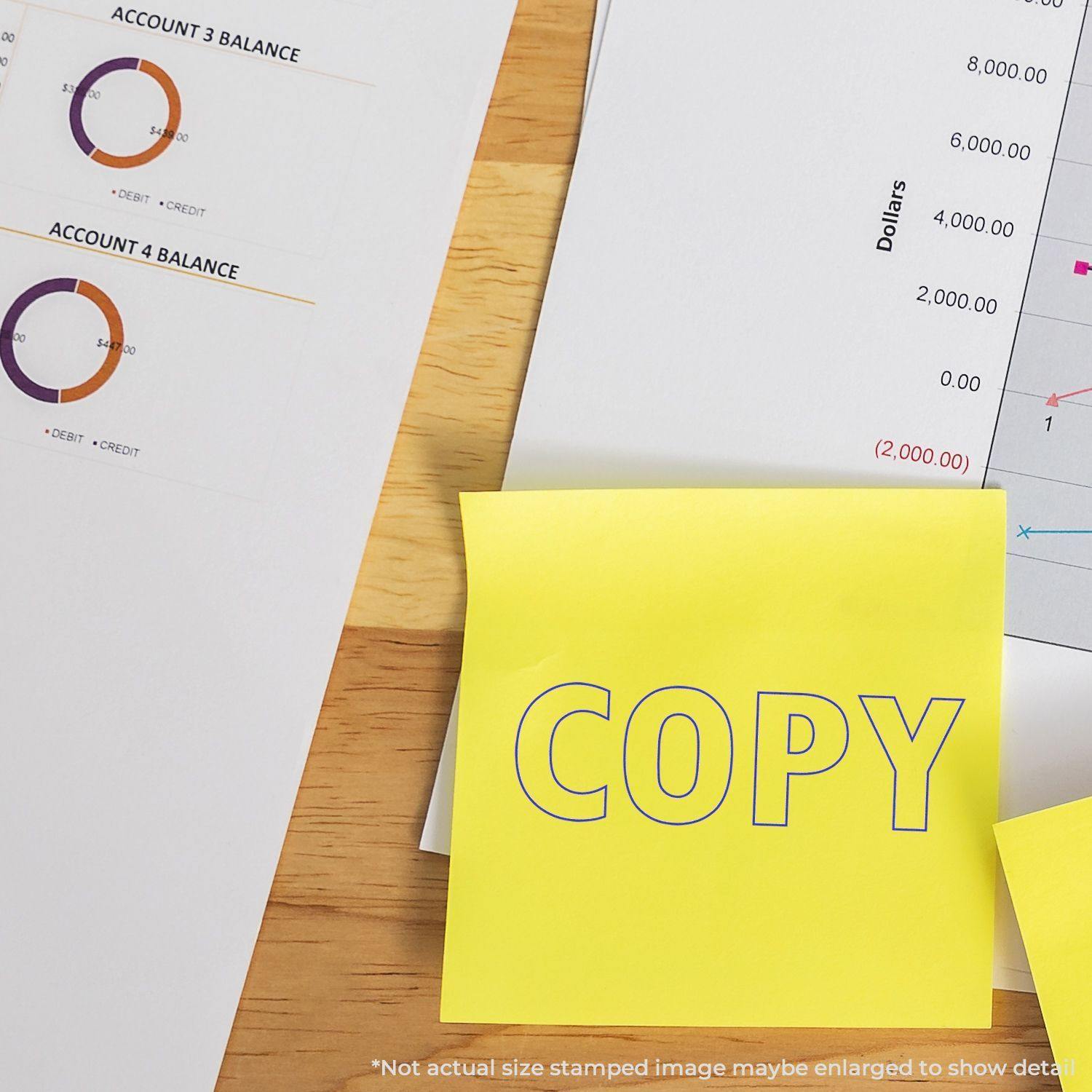 Large Outline Copy Rubber Stamp used on a yellow sticky note, placed on a desk with financial documents and charts in the background.