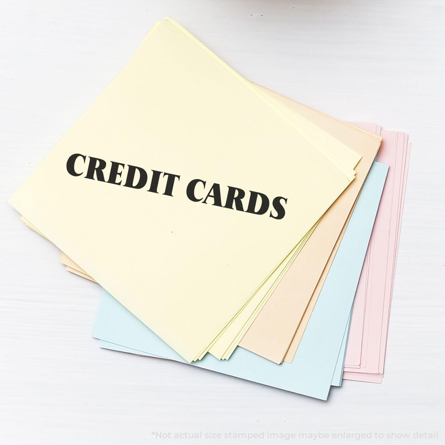 A stack of pastel-colored papers stamped with CREDIT CARDS using the Credit Cards Rubber Stamp, displayed on a white surface.