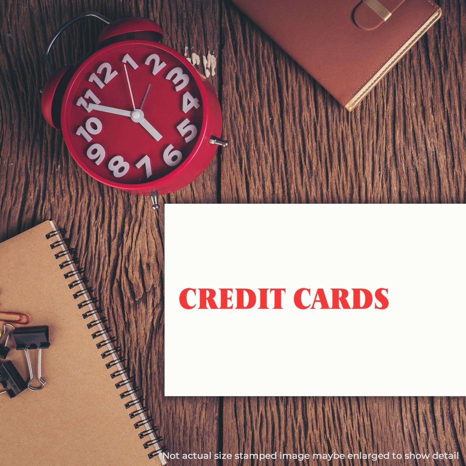 A red alarm clock, notebook, and office supplies on a wooden desk with a paper stamped CREDIT CARDS using the Credit Cards Rubber Stamp.