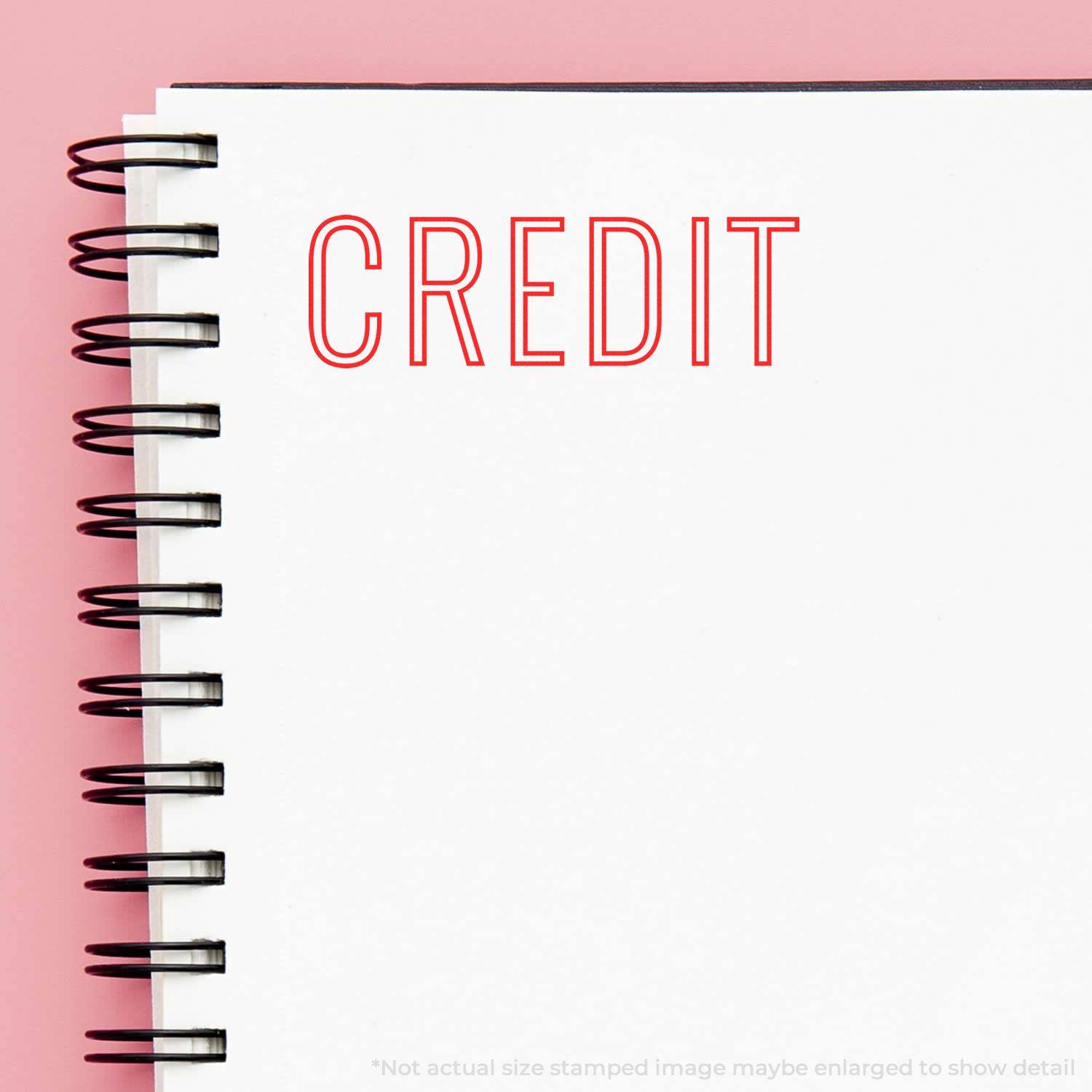 Credit Outline Rubber Stamp used on a white spiral notebook, displaying the word 'CREDIT' in red outline text on a pink background.