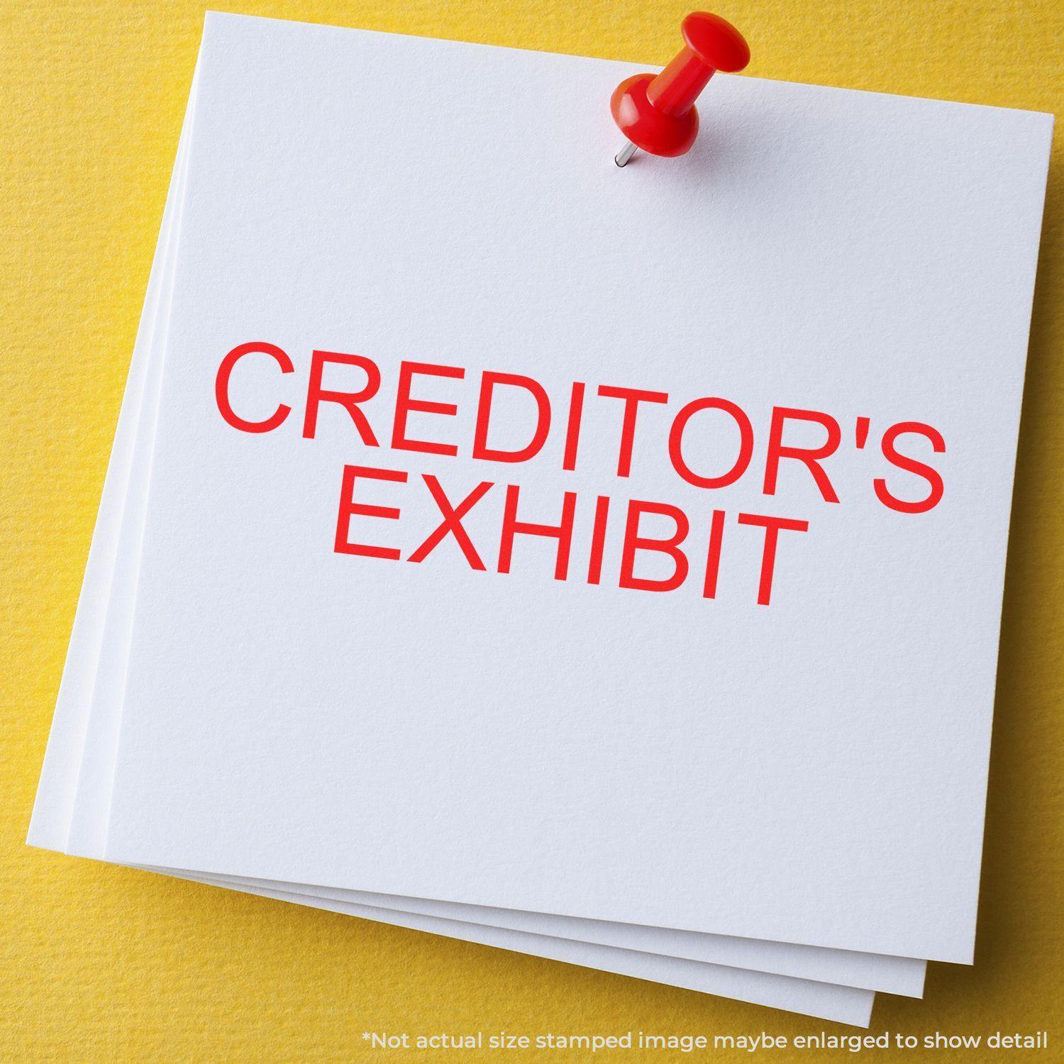 Slim Pre-Inked Creditors Exhibit Stamp in red ink on white paper, pinned with a red pushpin on a yellow background.