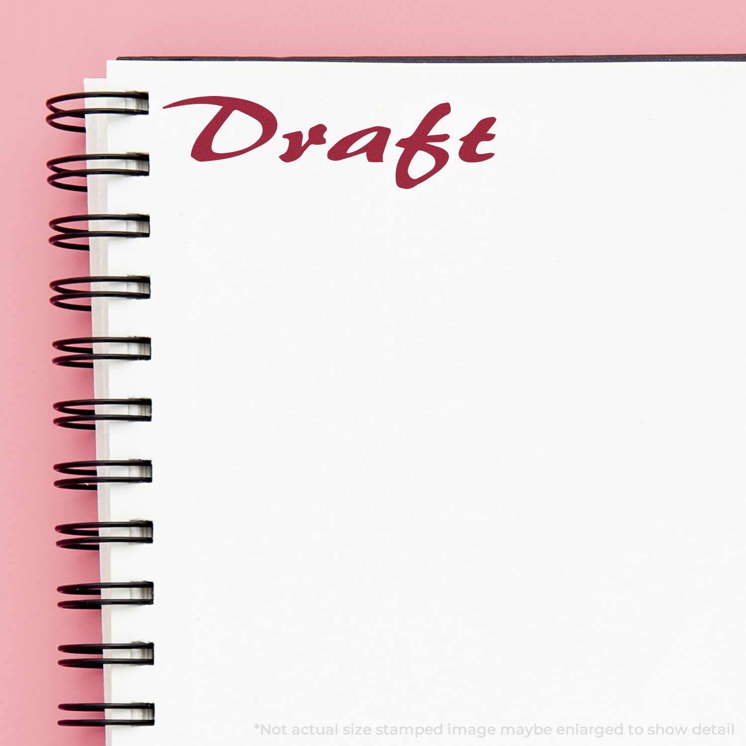 A notebook with a spiral binding and a Draft mark in red ink from the Cursive Draft Rubber Stamp on a pink background.