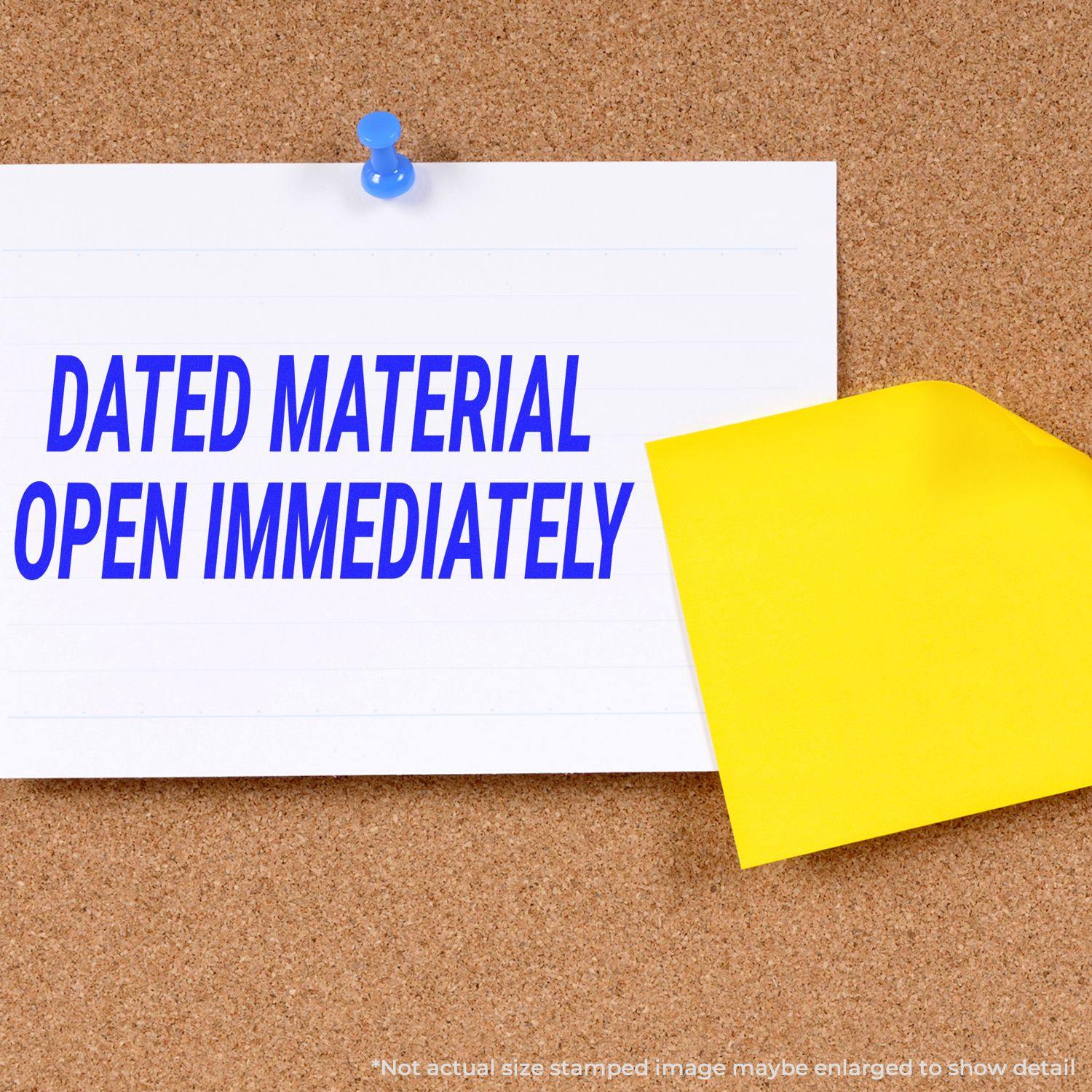 A corkboard with a white note stamped Dated Material Open Immediately Rubber Stamp in blue ink, pinned with a blue pushpin and a yellow sticky note.