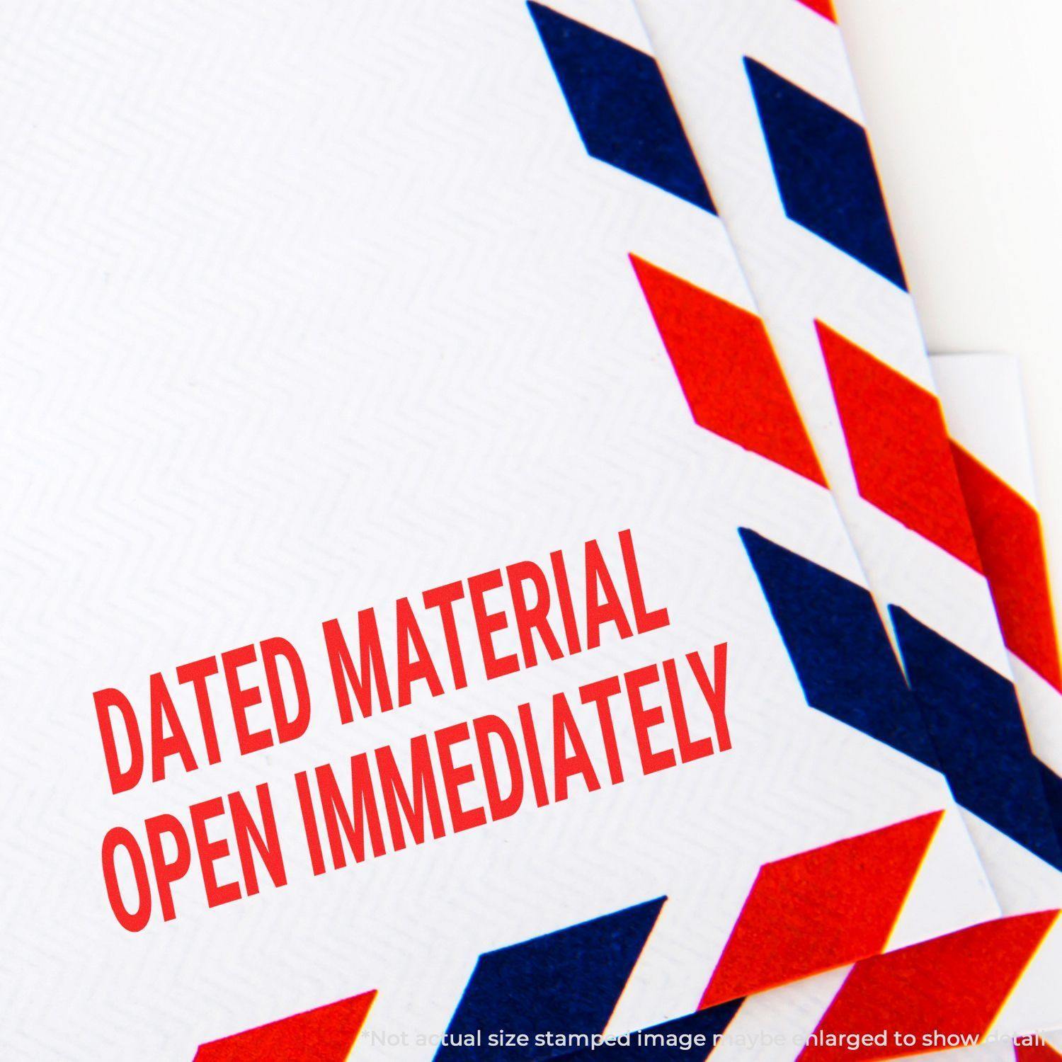 Close-up of an envelope stamped with Dated Material Open Immediately Rubber Stamp in red ink, surrounded by red and blue chevron patterns.