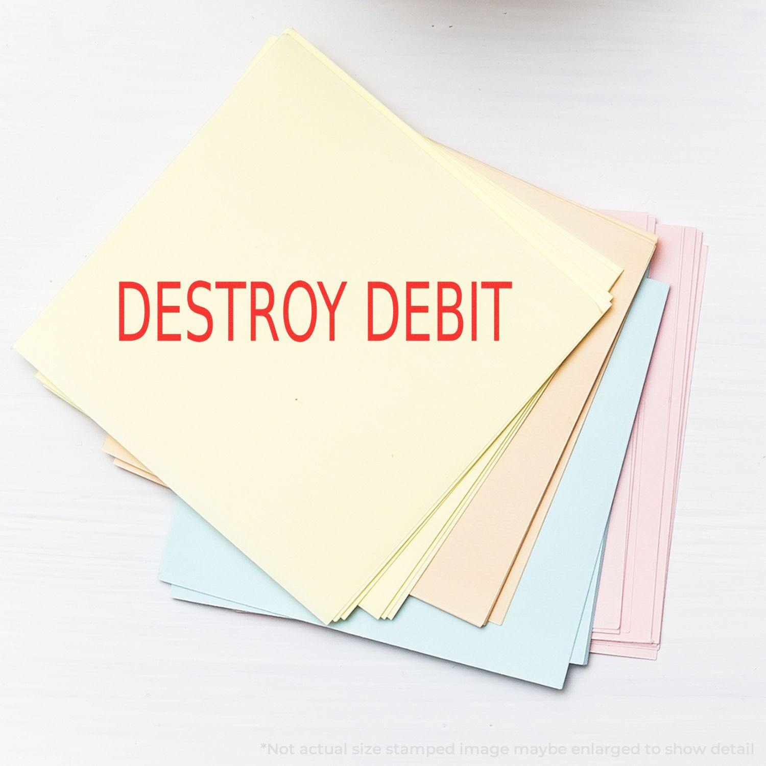 A stack of pastel-colored papers stamped with DESTROY DEBIT using the Large Pre-Inked Destroy Debit Stamp, placed on a white surface.