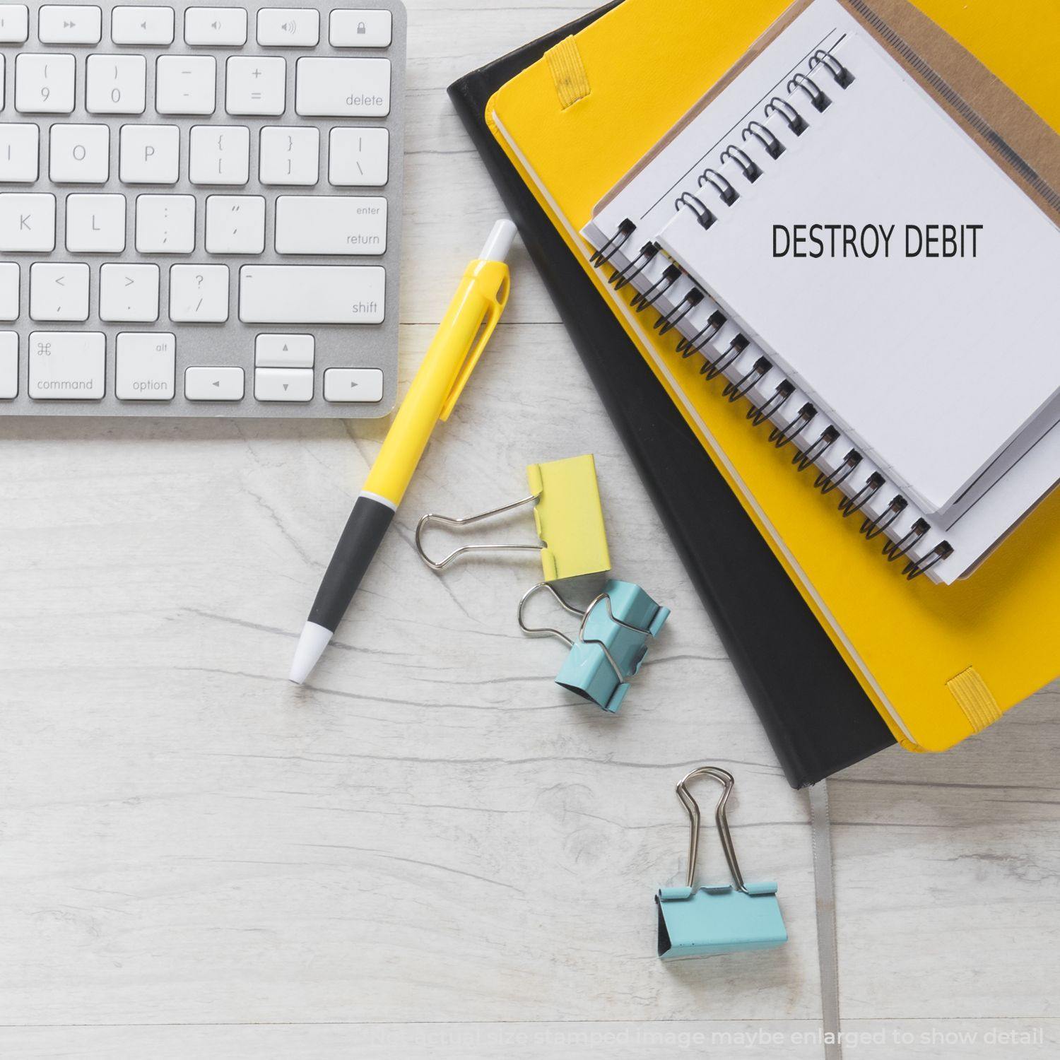 Yellow notepad with Destroy Debit rubber stamp, pen, keyboard, and binder clips on a desk.