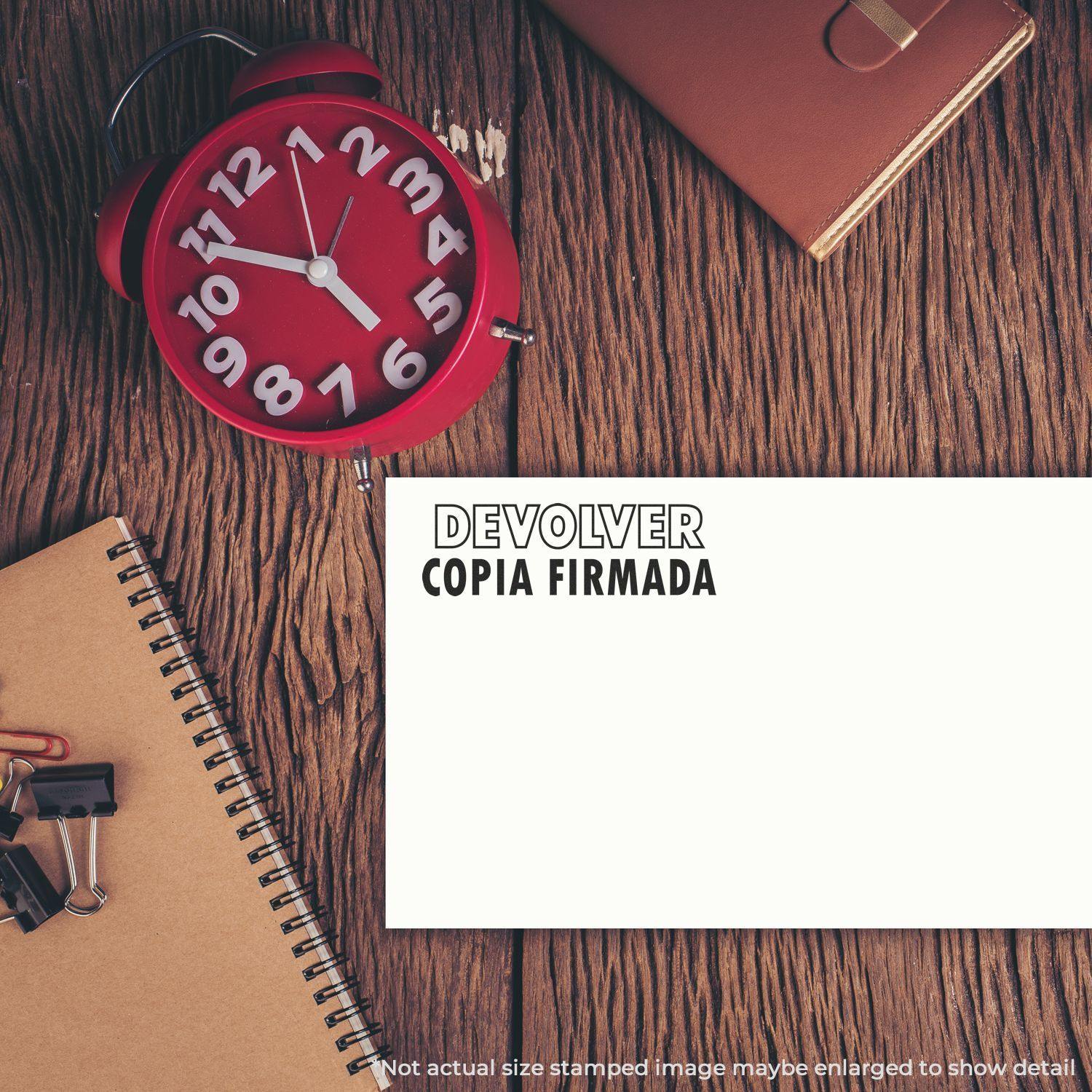 A Devolver Copia Rubber Stamp is used on a white paper, placed on a wooden desk with a red clock, notebook, and office supplies.