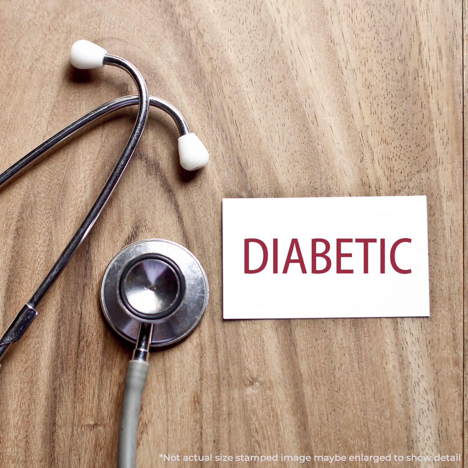 Self Inking Diabetic Stamp next to a stethoscope on a wooden surface, with the word DIABETIC stamped in red on a white card.