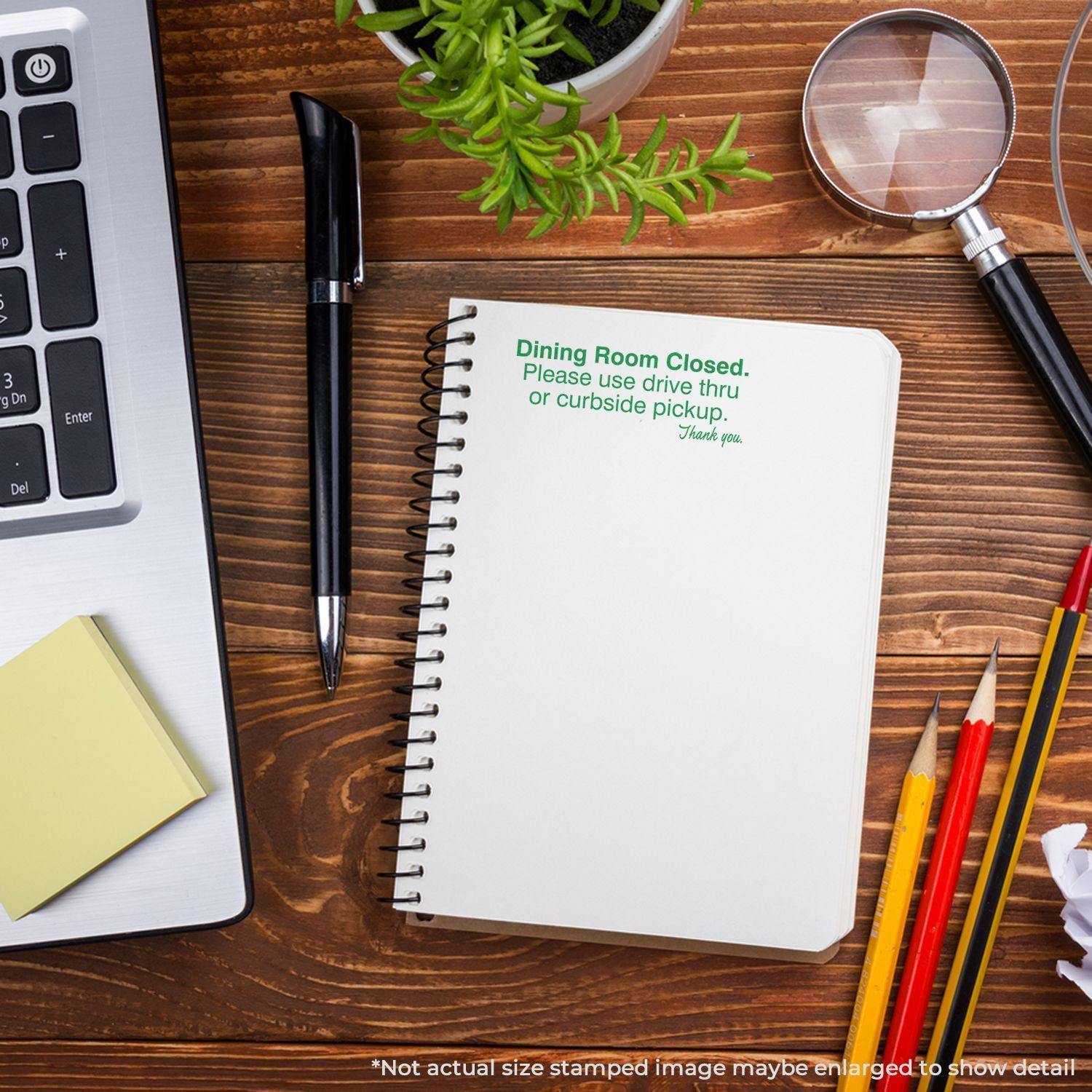 Dining Room Closed Rubber Stamp on a notebook, surrounded by office supplies, a laptop, and a plant on a wooden desk.