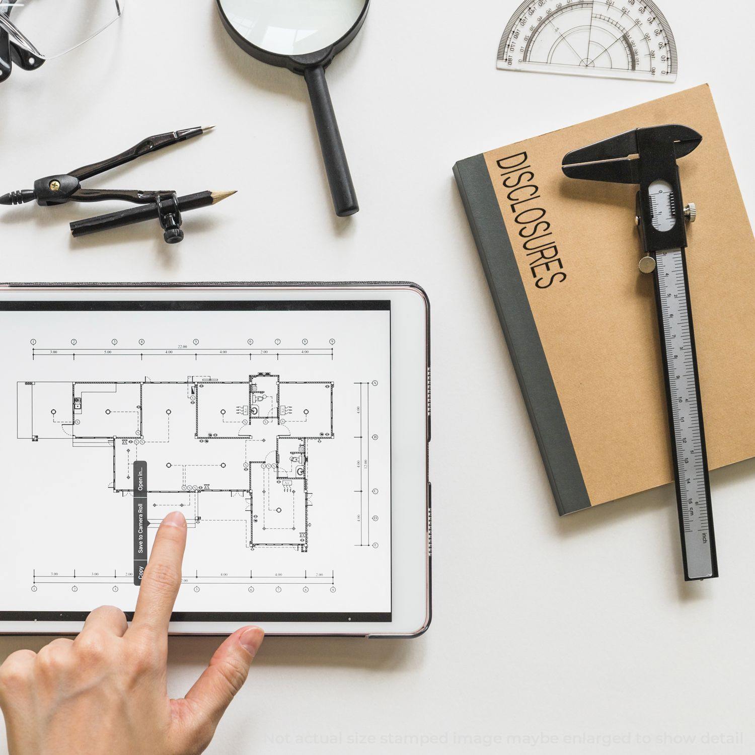 A Disclosures Rubber Stamp is placed on a notebook beside drafting tools, a tablet displaying a floor plan, and a hand pointing at the screen.