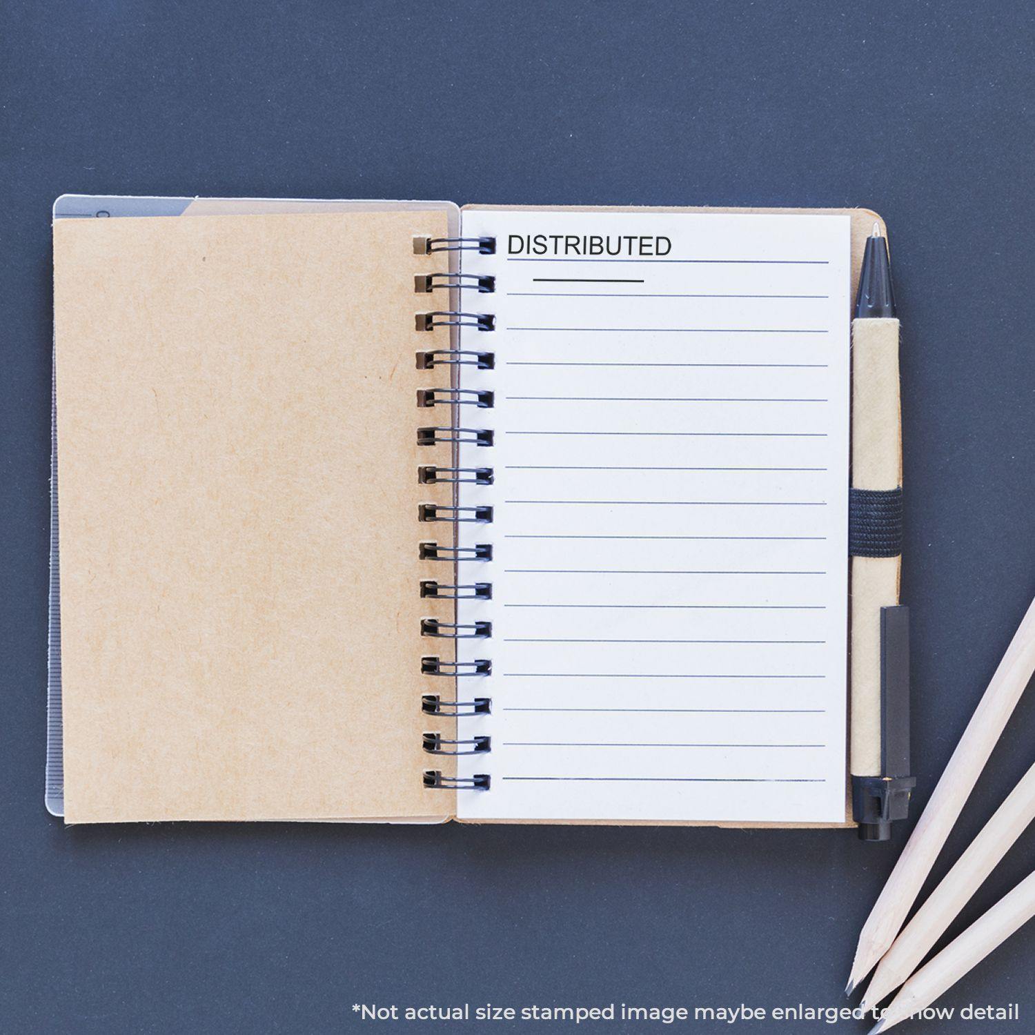 A notebook with a DISTRIBUTED stamp impression on a lined page, created using the Distributed Rubber Stamp, with a pen and pencils nearby.