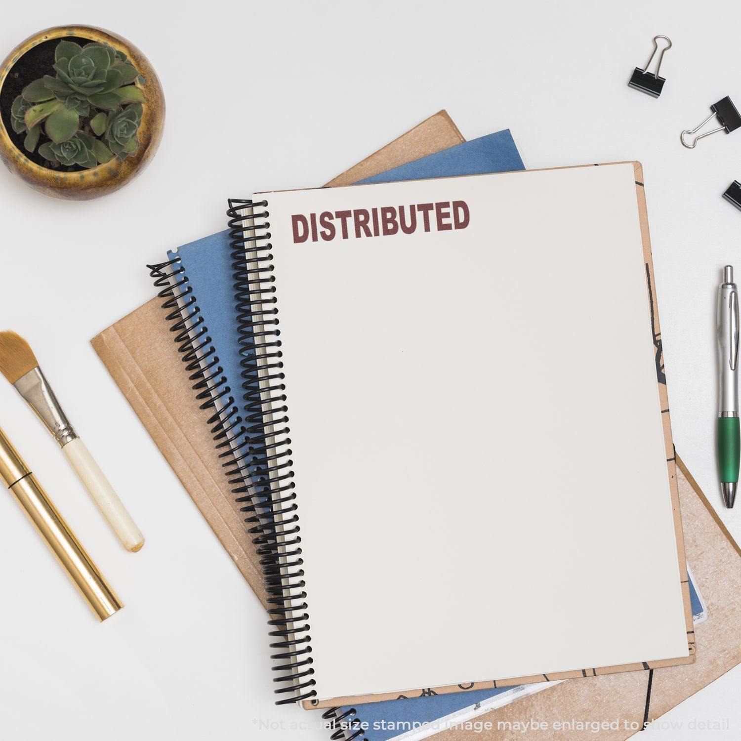 A notebook stamped with DISTRIBUTED using the Distributed Rubber Stamp, surrounded by office supplies including pens, clips, and a plant.