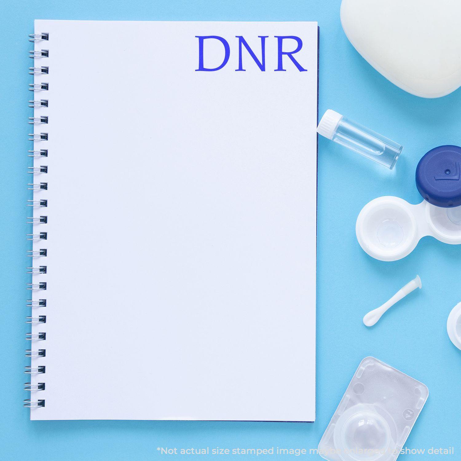 A DNR Medical Rubber Stamp imprint on a white notebook, surrounded by medical supplies on a blue background.