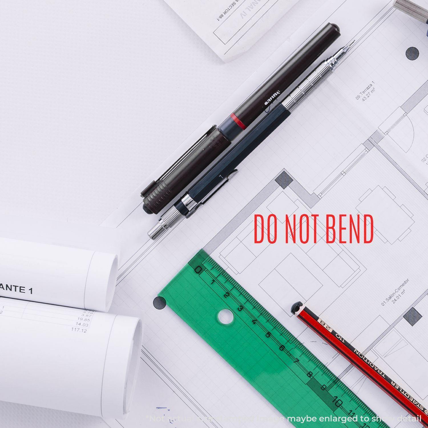 Do Not Bend Rubber Stamp used on architectural plans with pens, ruler, and rolled blueprints on a white desk.