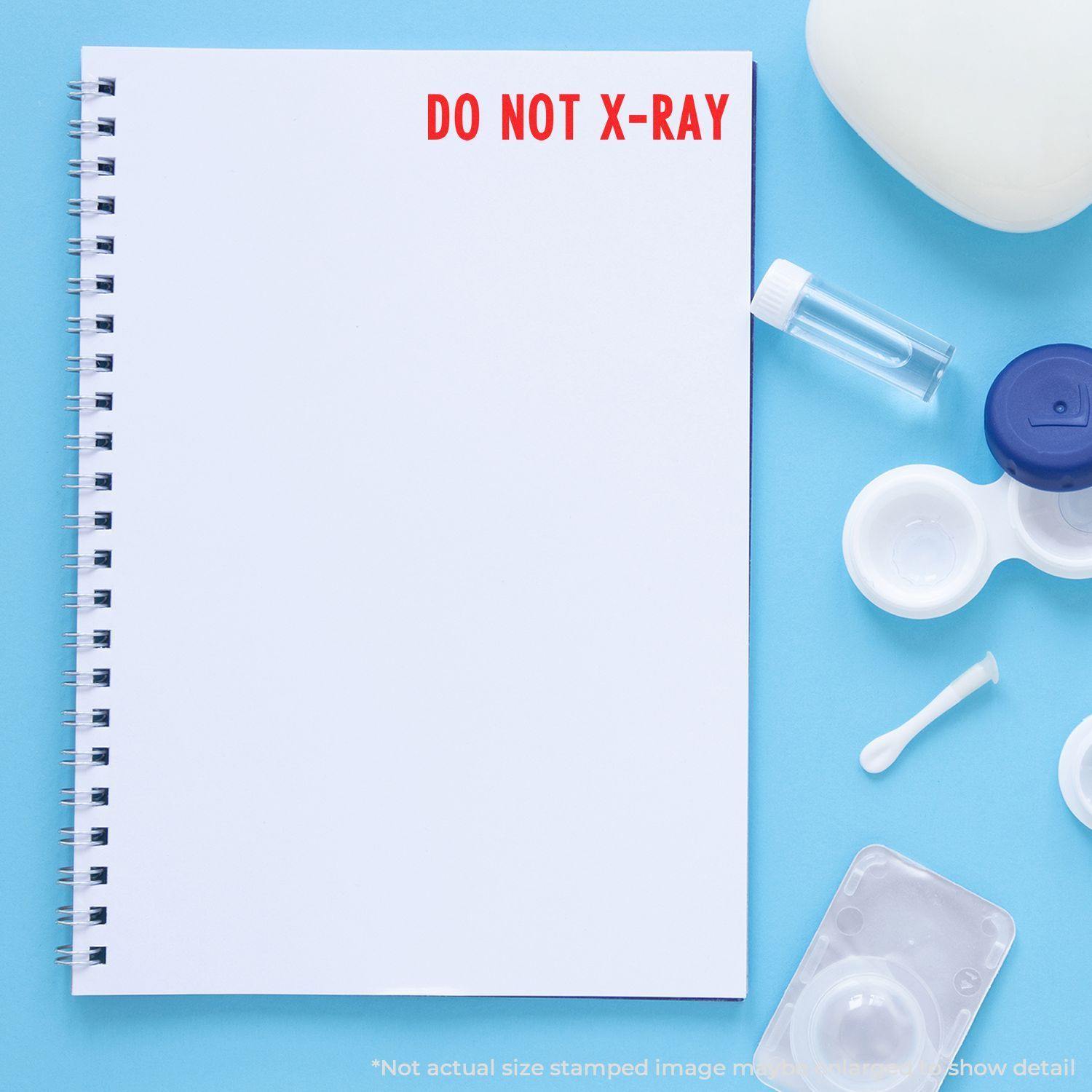 Large Pre-Inked Do Not X-Ray Stamp used on a white notebook page, surrounded by medical items on a blue background.