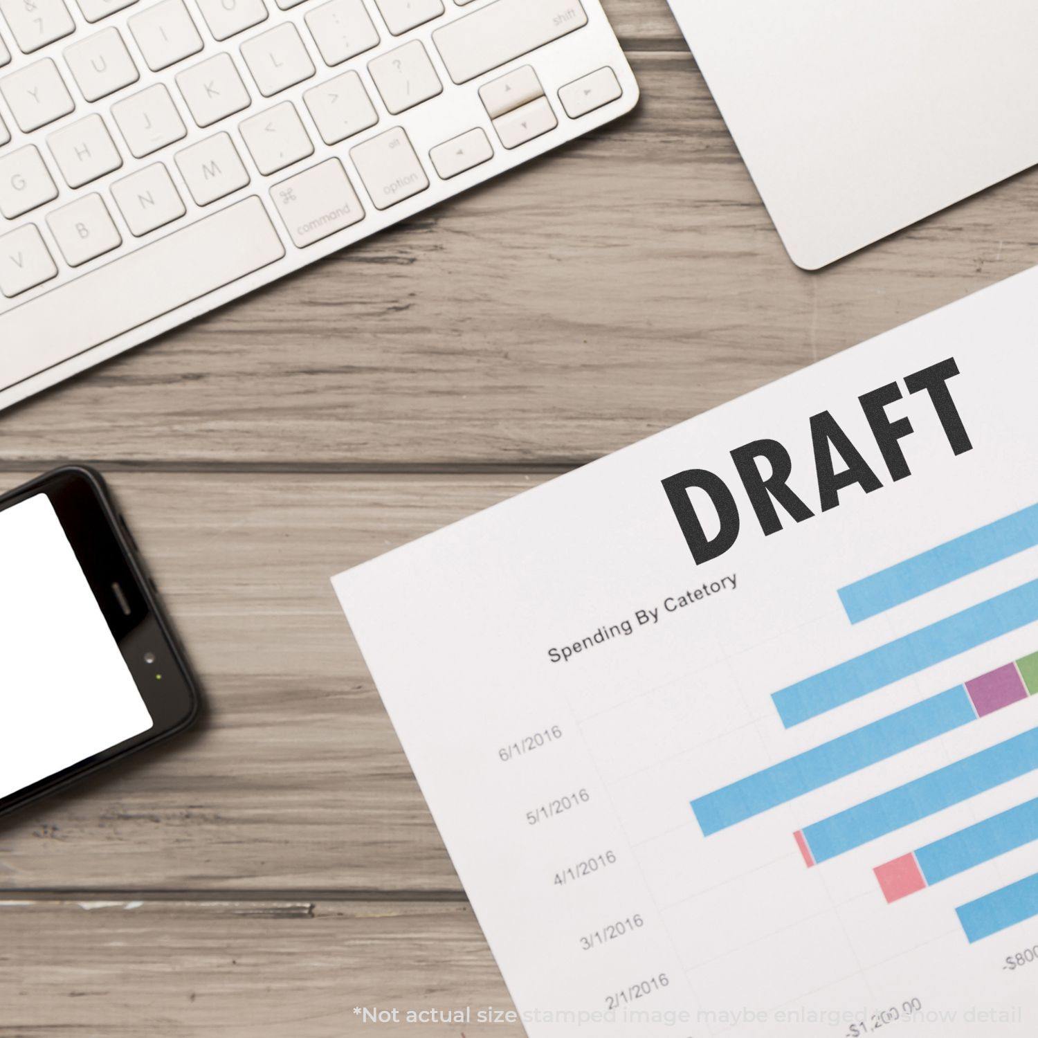 A Large Draft Rubber Stamp is used on a document with charts, placed on a wooden desk next to a keyboard and smartphone.