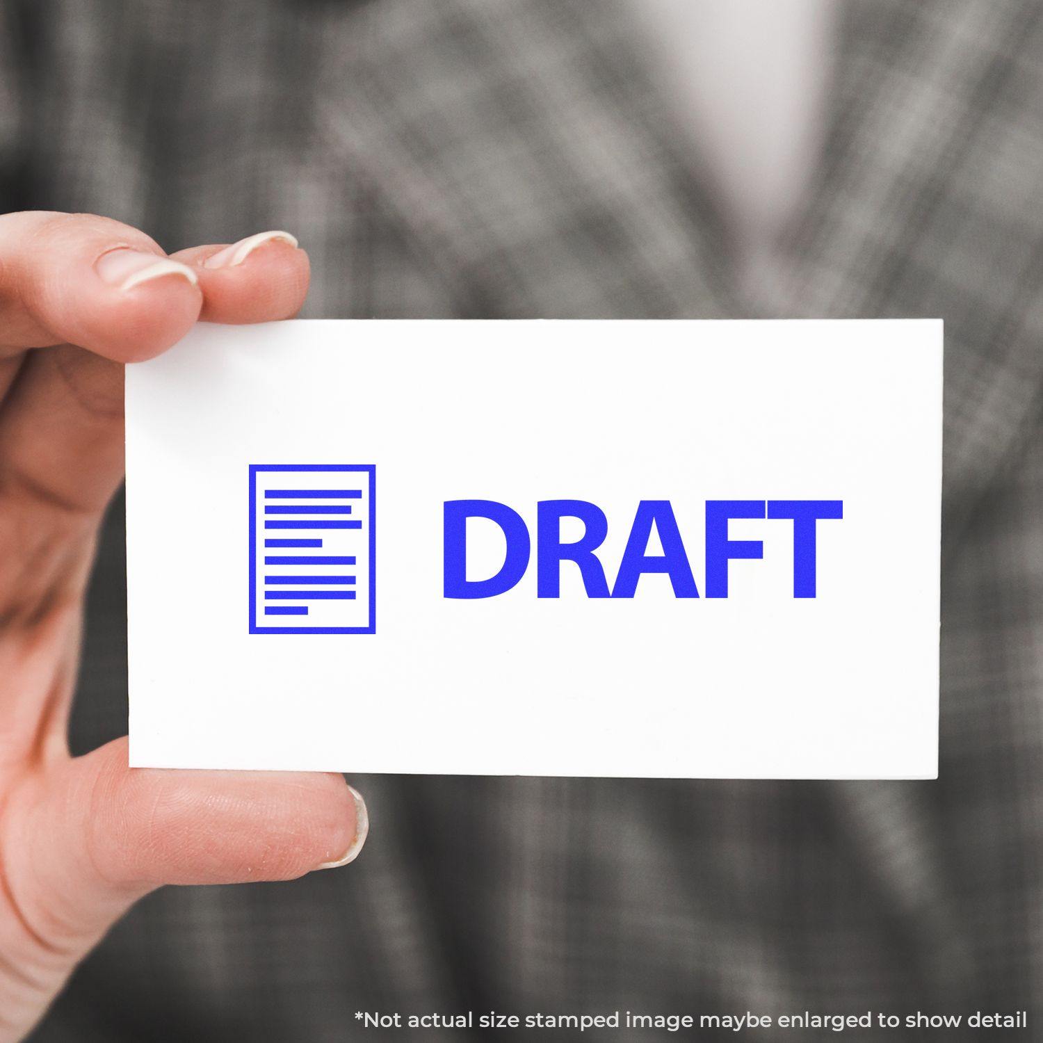 A hand holding a white card stamped with DRAFT in blue using the Draft with Letter Rubber Stamp. Background shows a blurred plaid pattern.