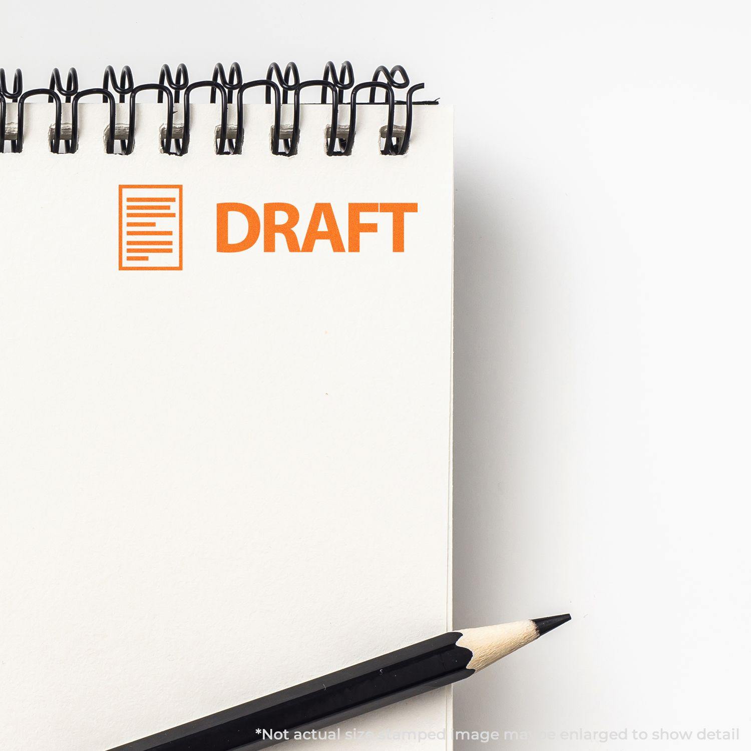 A Large Pre-Inked Draft with Letter Stamp imprinting DRAFT in orange on a spiral notebook, with a pencil placed beside it.