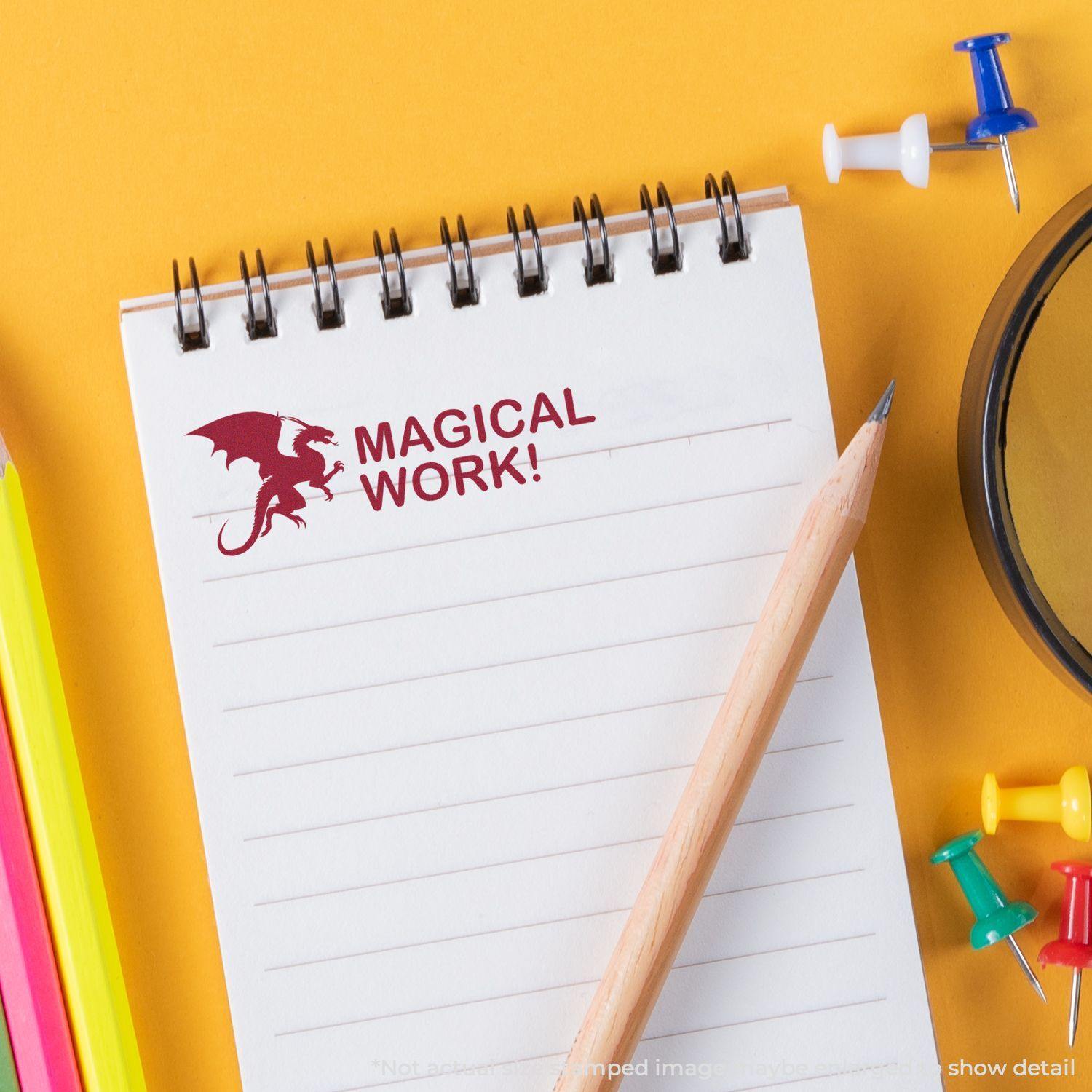 A notepad stamped with Dragon Magical Work Rubber Stamp in red ink, surrounded by a pencil, colorful pens, and push pins on a yellow background.