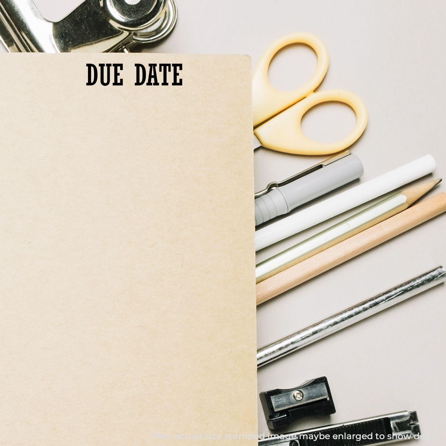 Large Due Date Rubber Stamp marking DUE DATE on a brown folder, surrounded by office supplies like scissors, pens, and pencils.