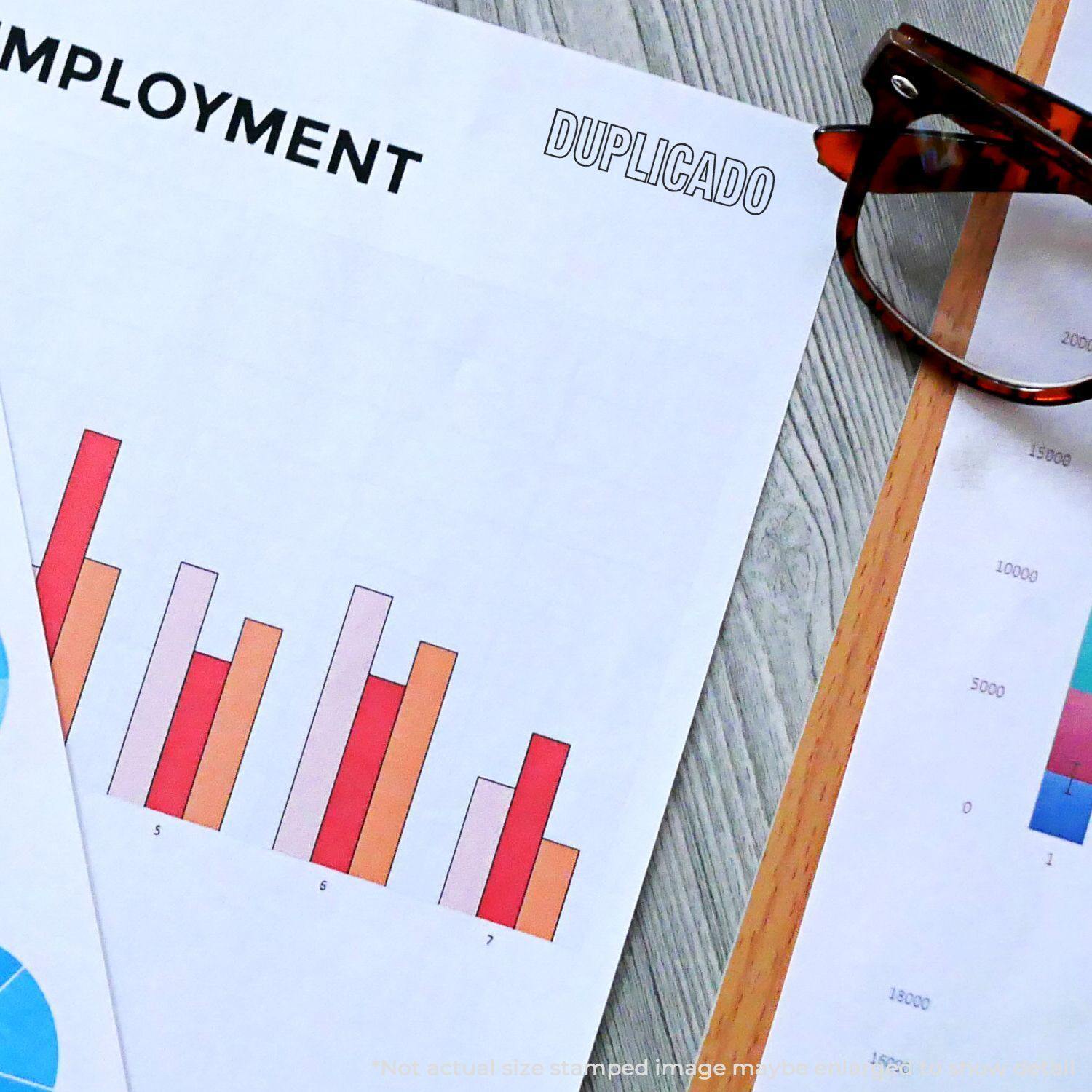 A Duplicado Rubber Stamp is used on a document with charts and graphs, next to a pair of glasses on a wooden desk.