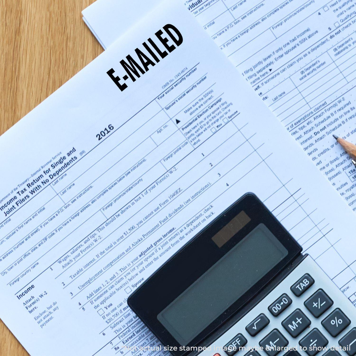 A Large Self Inking E Mailed Stamp marks a tax document, with a calculator and pencil nearby on a wooden desk.