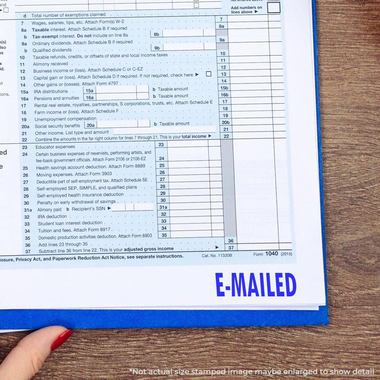 A hand holding a Slim Pre-Inked E-Mailed Stamp, stamping E-MAILED in blue ink on a tax document.